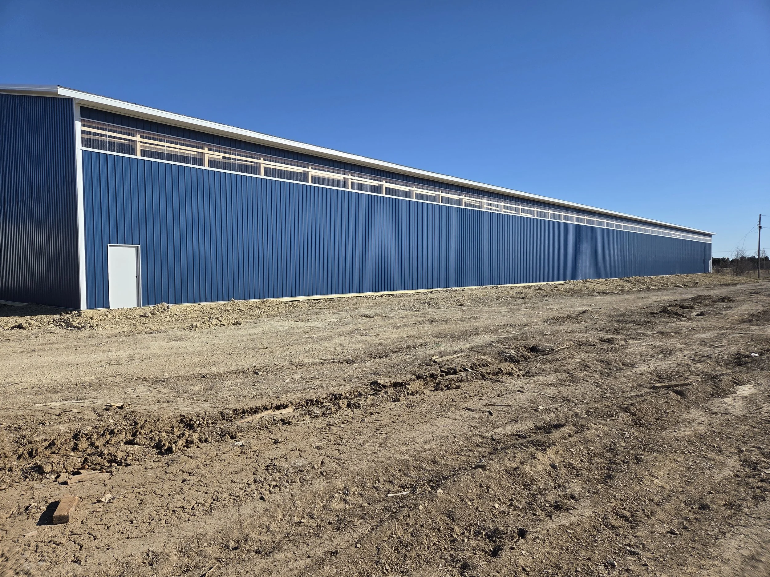 Large blue industrial building on a dirt lot under a clear blue sky.