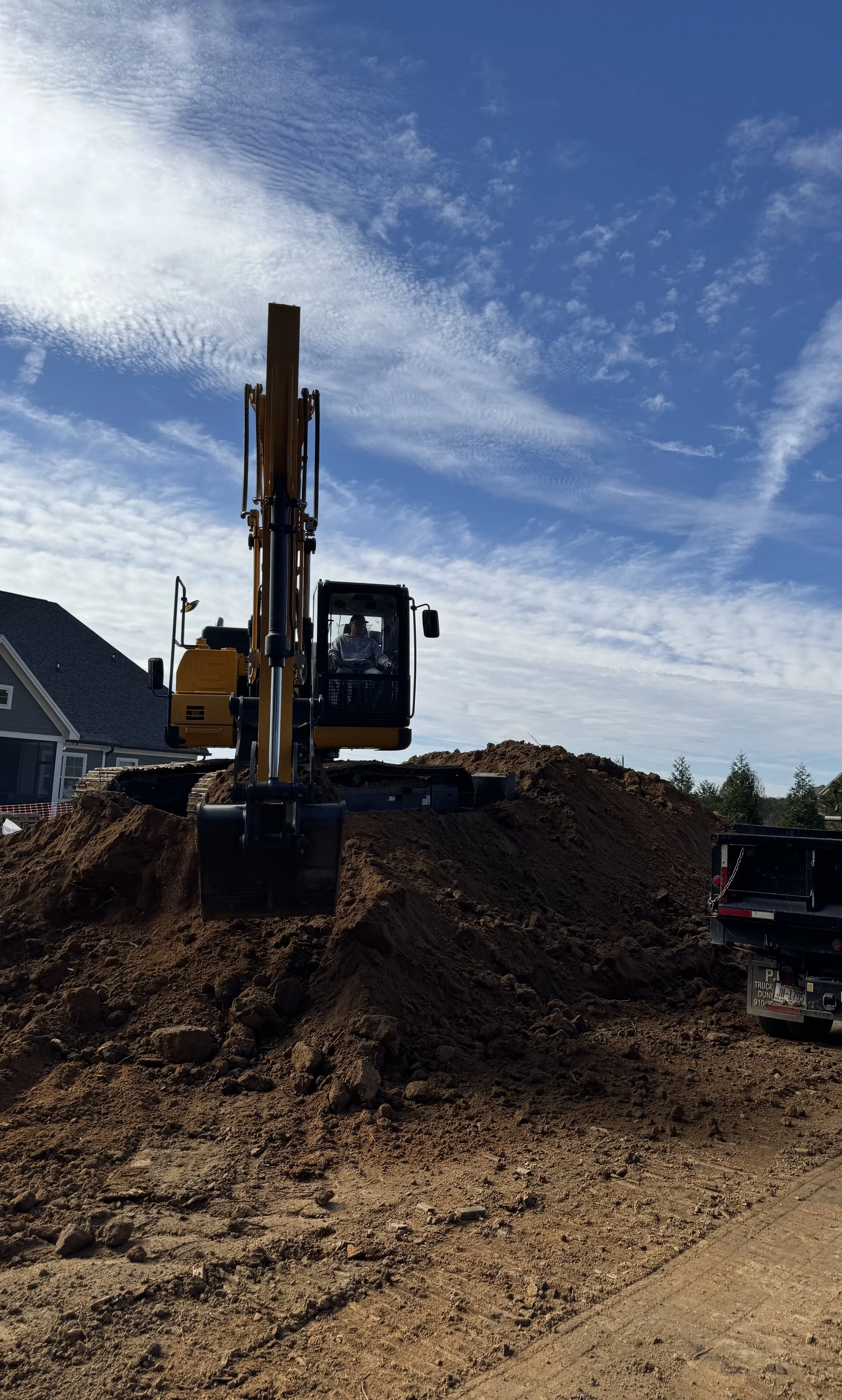 A construction excavator working on a mound of dirt at a building site with a partly cloudy sky overhead.