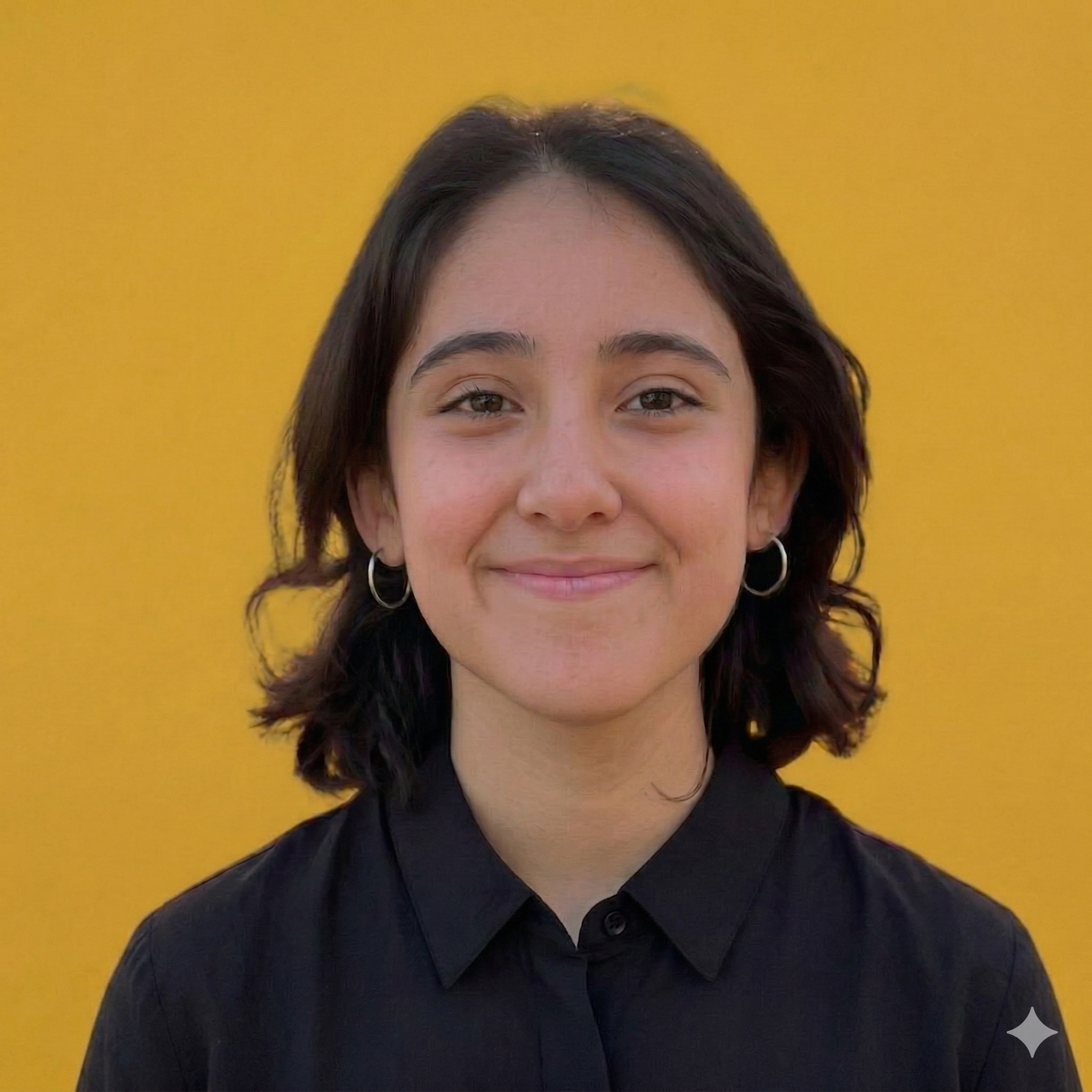 Young woman with short dark hair, earrings, wearing a black button-up shirt, smiling in front of a yellow background.