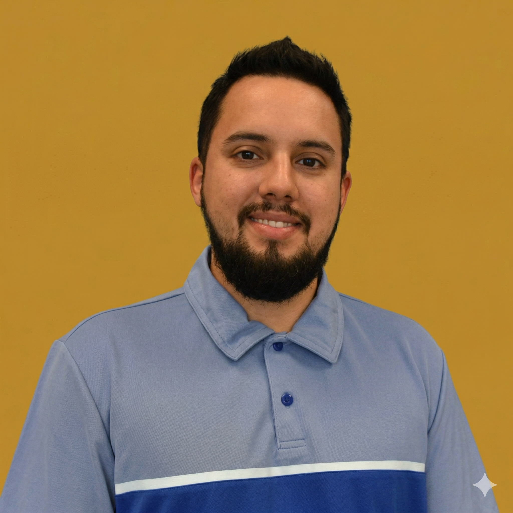 A young man with dark hair and a beard smiling, wearing a light blue polo shirt with a darker blue stripe, against a yellow background.