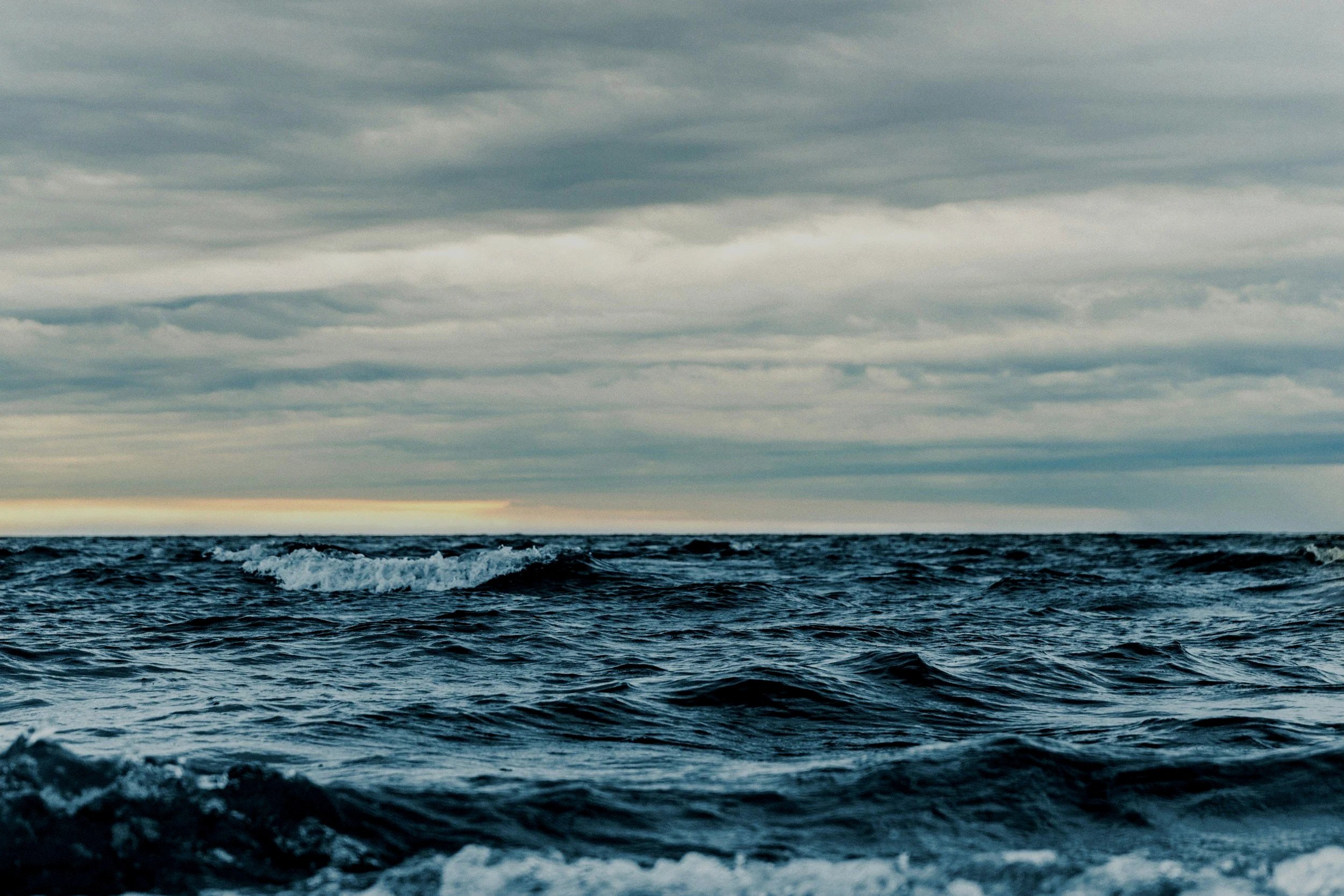 A vast ocean with dark, choppy waves under a cloudy sky, with the horizon line visible in the distance.