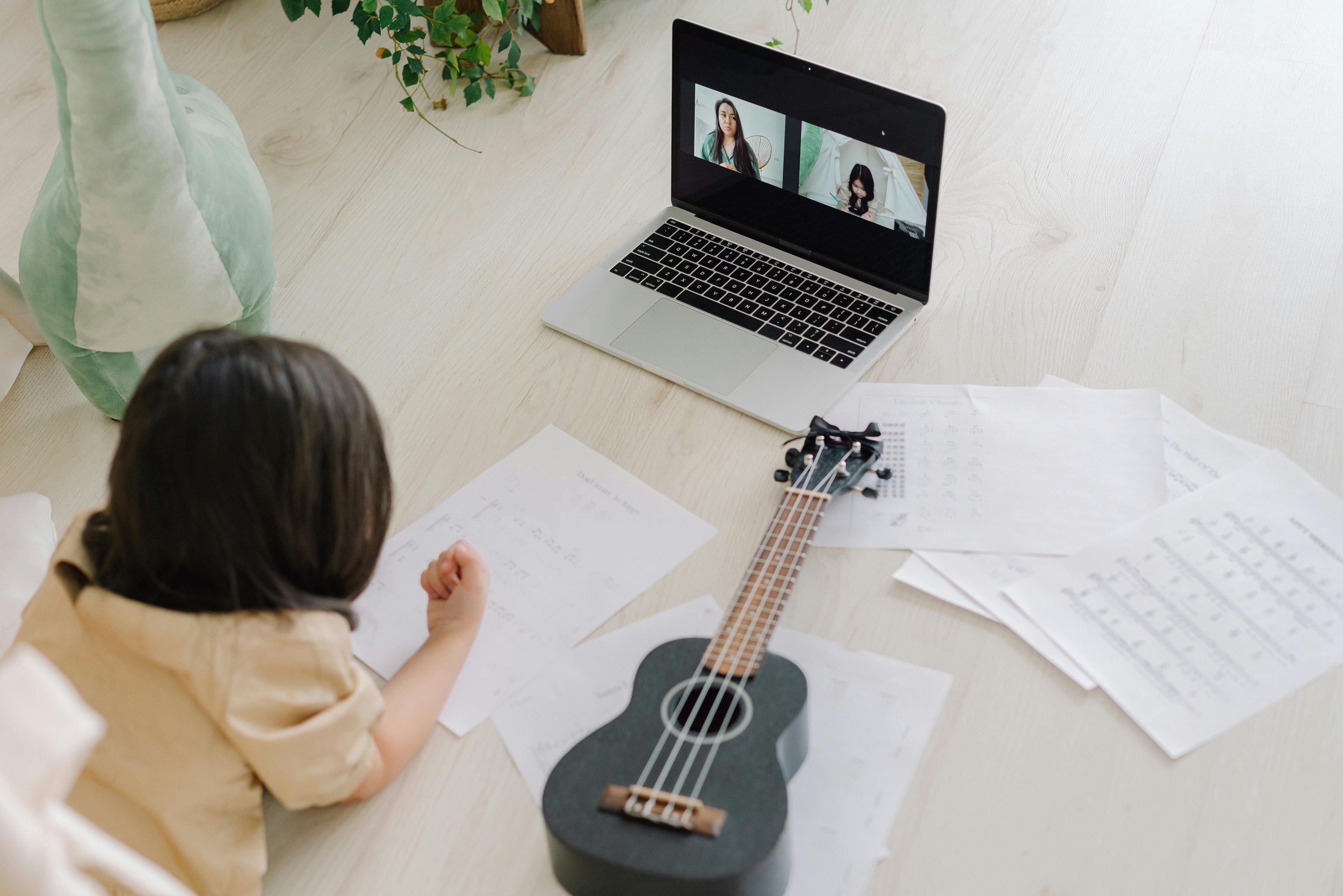 An online student laying on the floor with papers and a ukulele