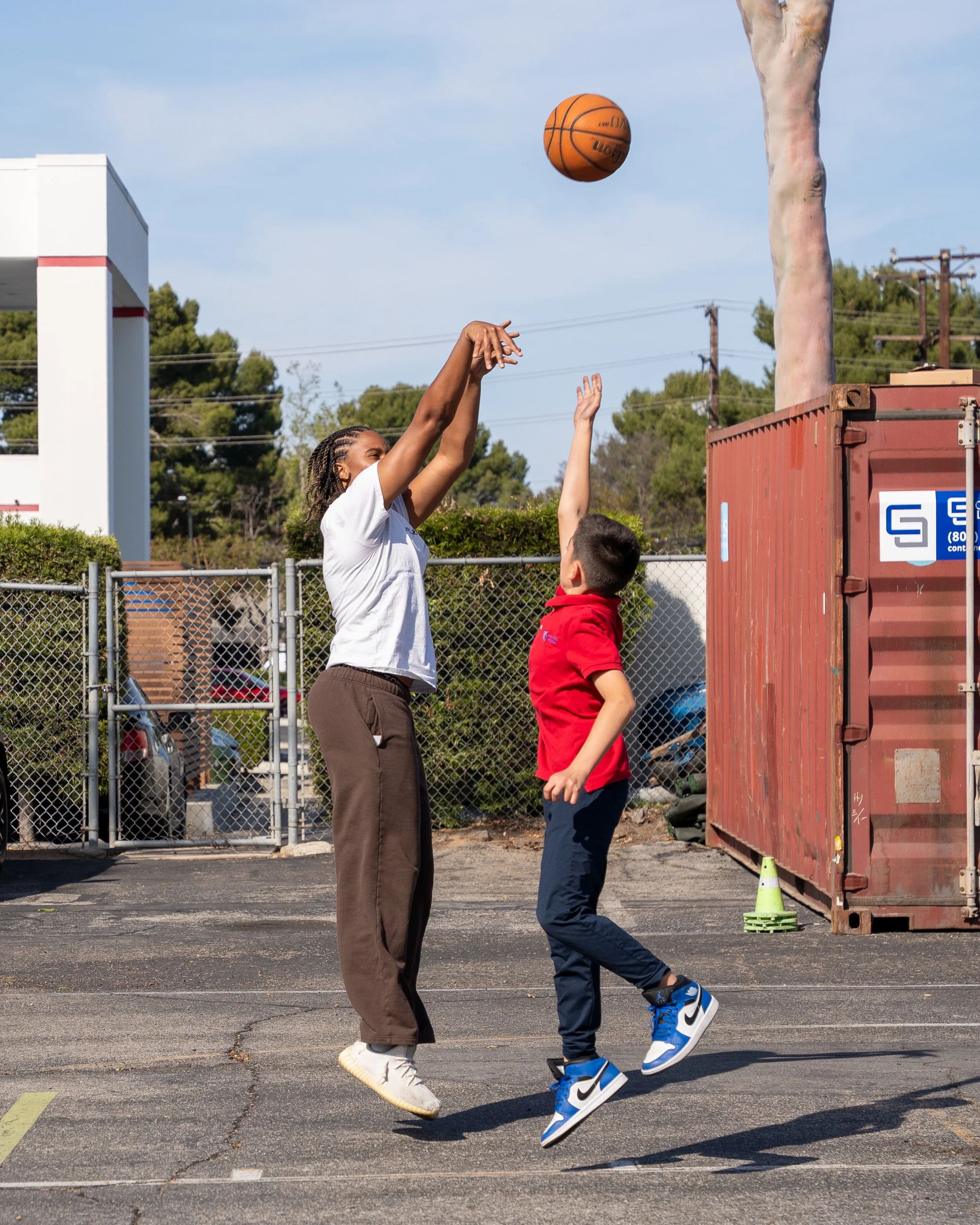 A woman coach and a boy playing basketball outdoors