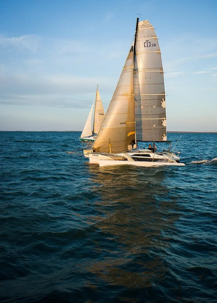 Two sailboats on the open water during a sunny day, with a clear sky and calm waves.