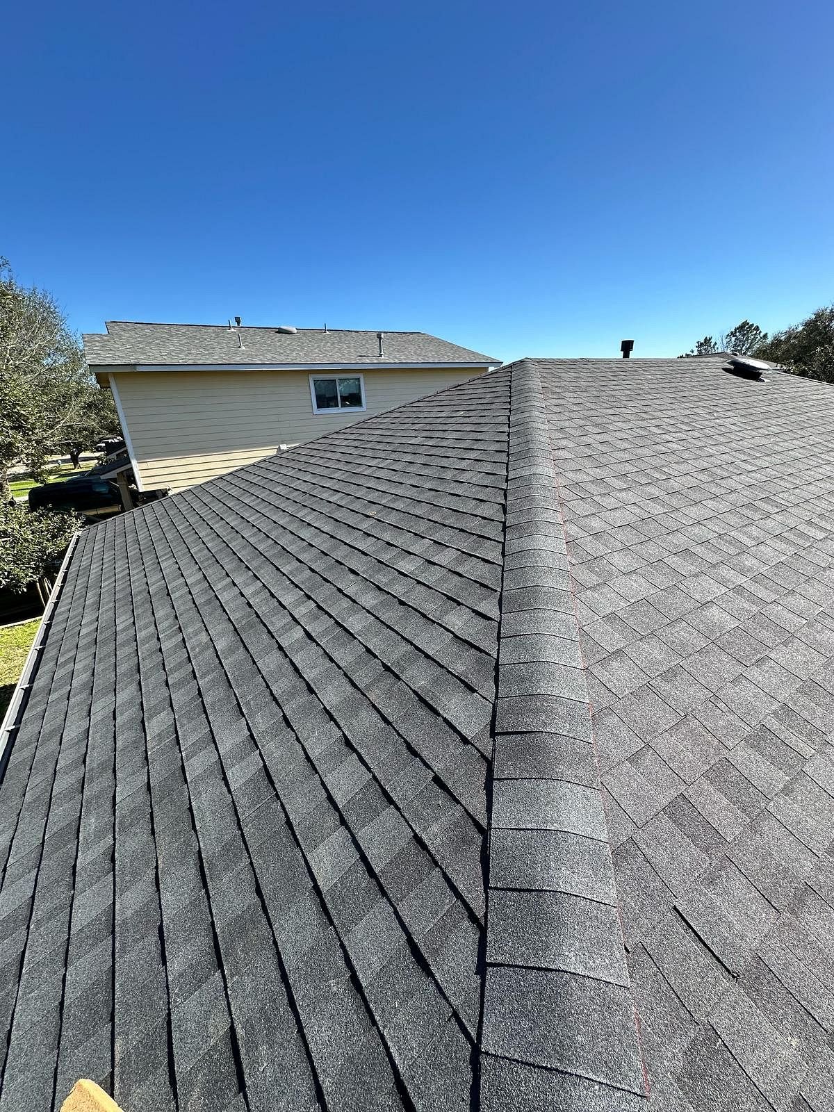 View of a residential roof with asphalt shingles under a clear blue sky.