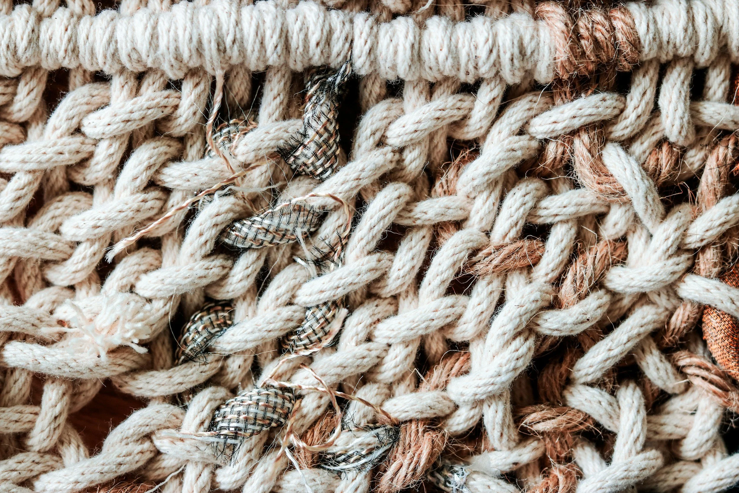 Close-up of tangled and worn ropes, with frayed fibers and some patterned fabric pieces caught in the strands.