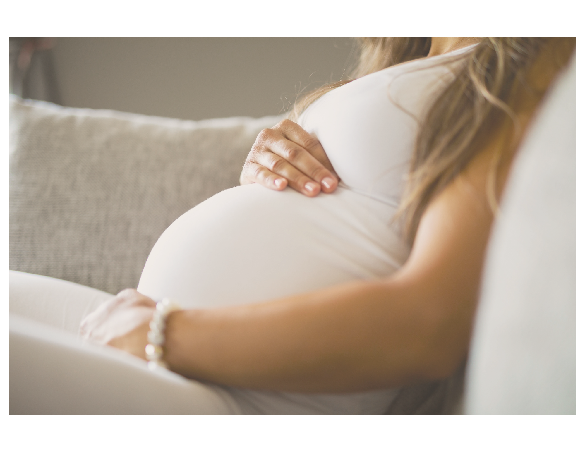 Pregnant woman sitting on a sofa with her hand resting on her belly.