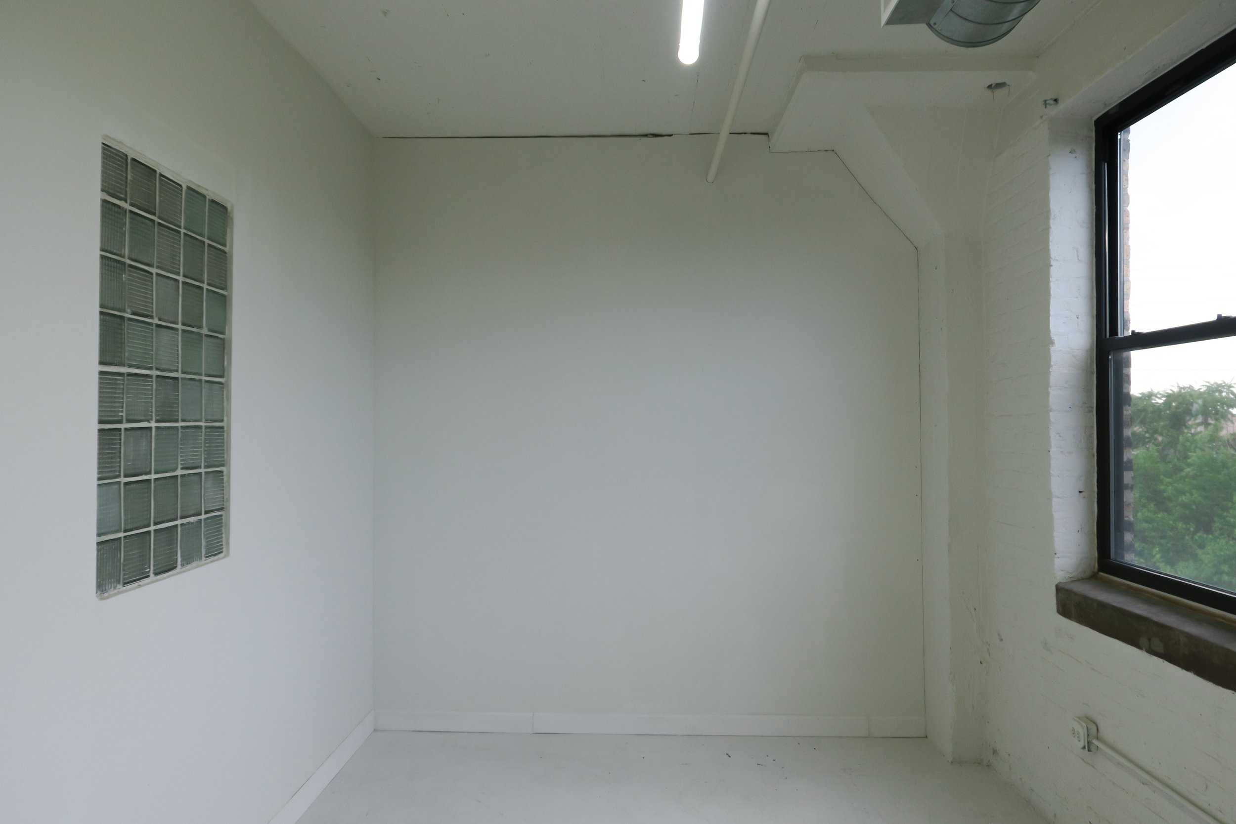 Empty white-walled room with a large window, glass block wall section, and ceiling light