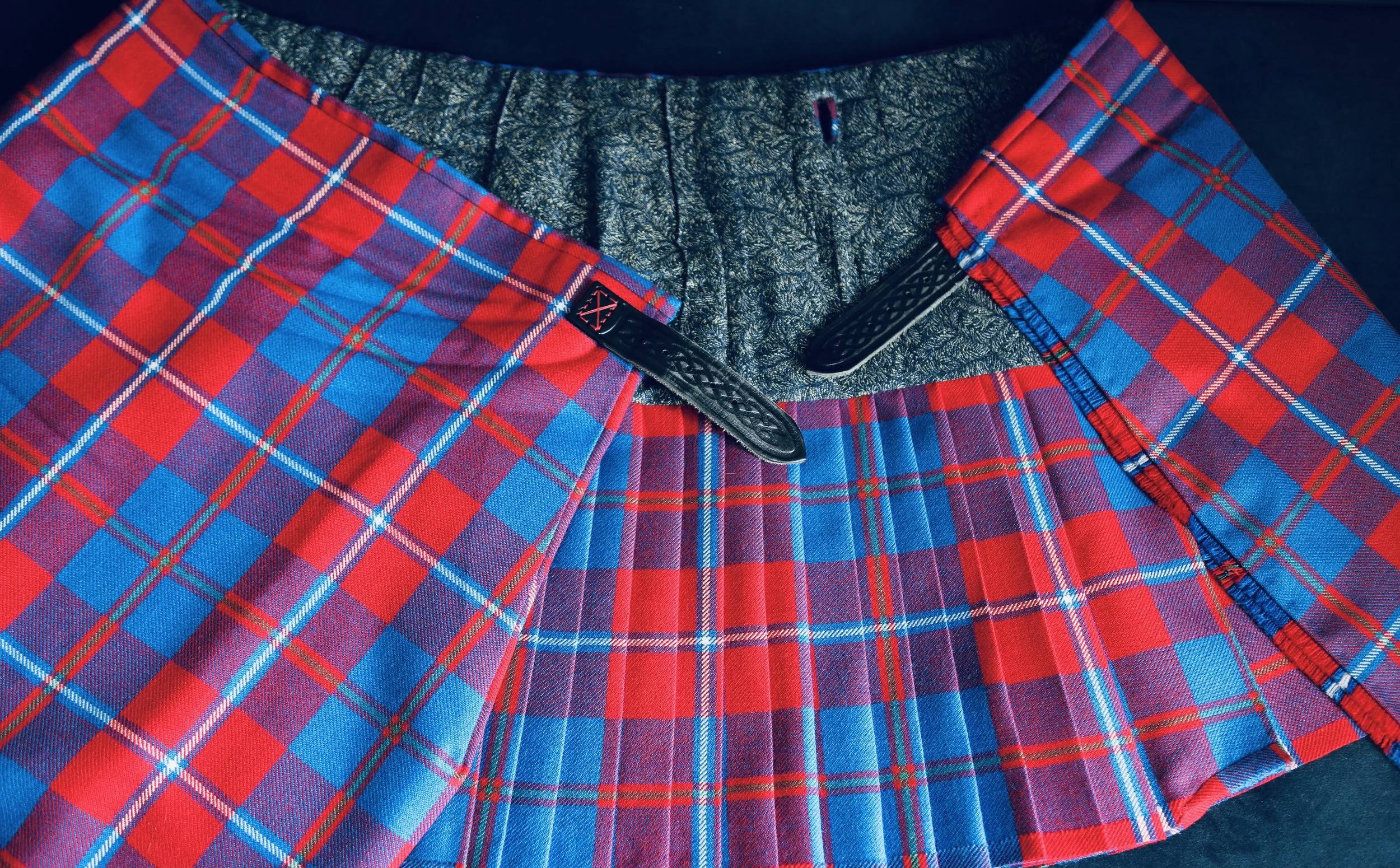 Close-up of red, blue, and green plaid tartan handmade kilt with a dark blue lining and black leather straps 