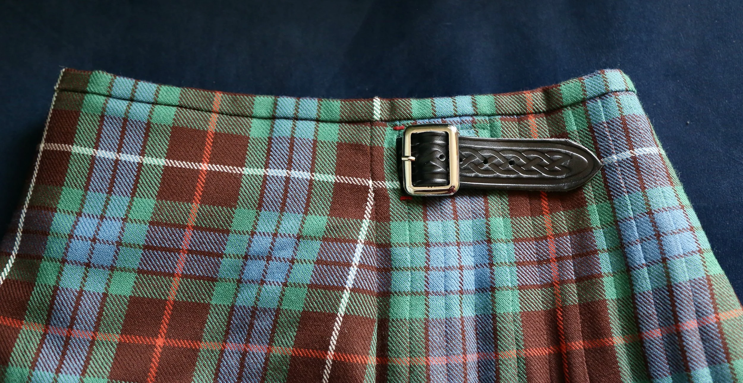 Close-up of a tartan plaid kilt with a decorative leather buckle.