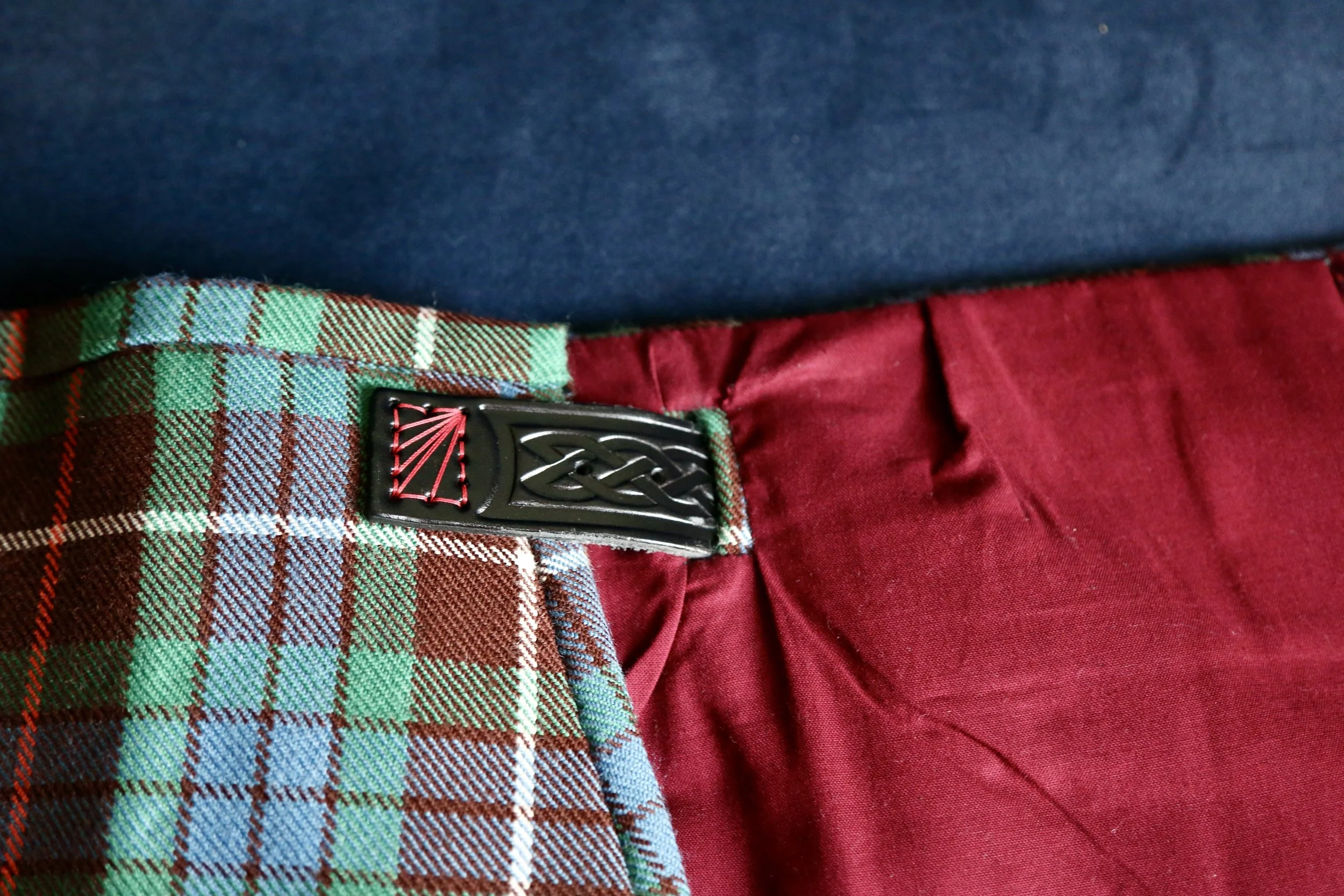 Close-up of a plaid tartan kilt with a black  strap with red decorative stitching