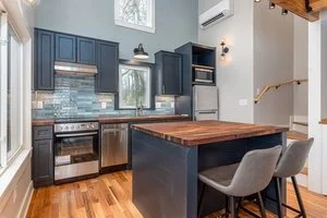 Kitchen with blue cabinets, a wooden kitchen island, gray chairs, and hardwood floors.