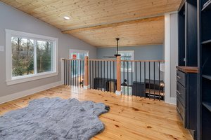 Living room with large window, wooden ceiling, hardwood floor, gray rug, and a staircase with black railing.