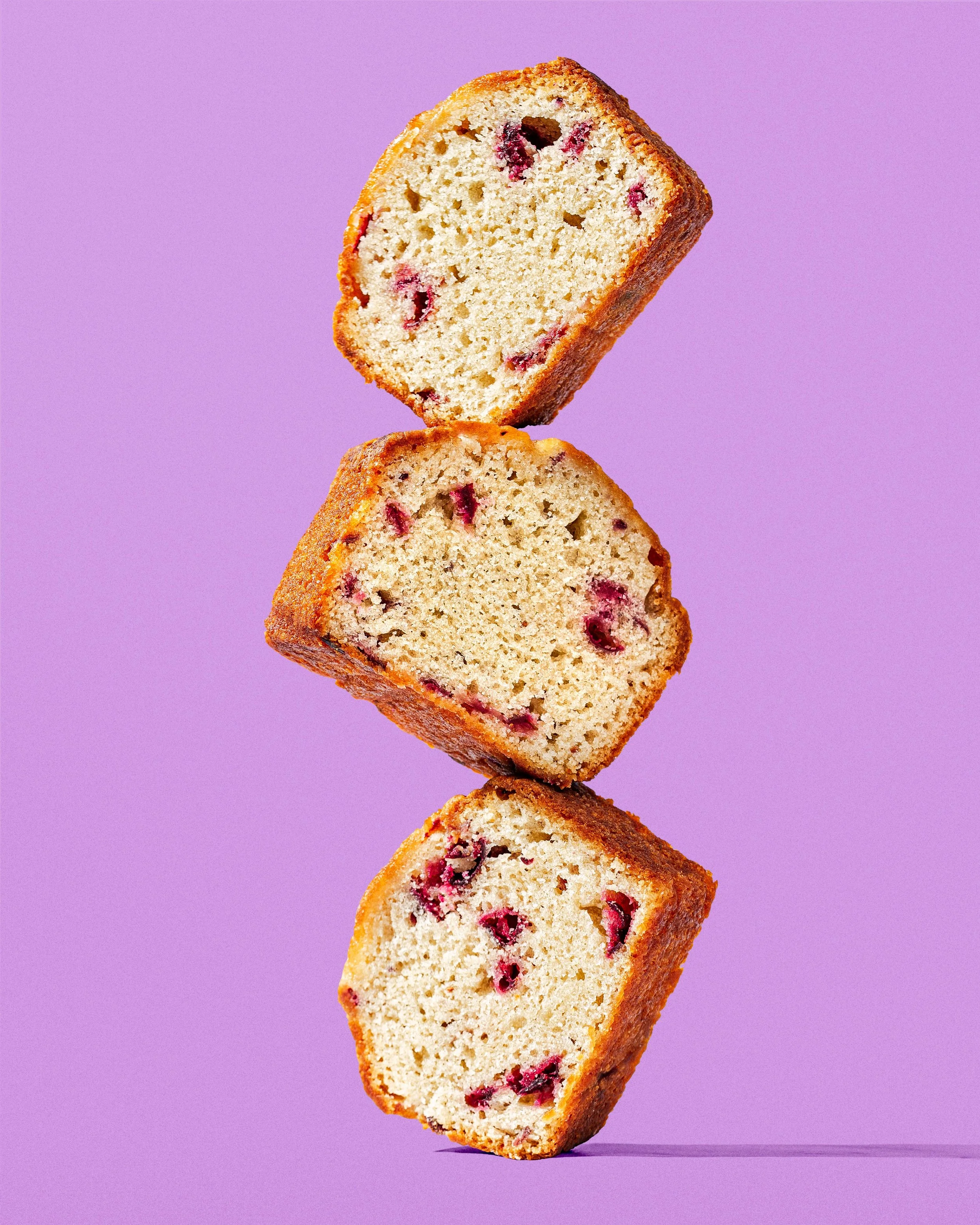 Slice of blueberry loaf cake with visible blueberries inside, stacked on top of two other slices against a purple background.