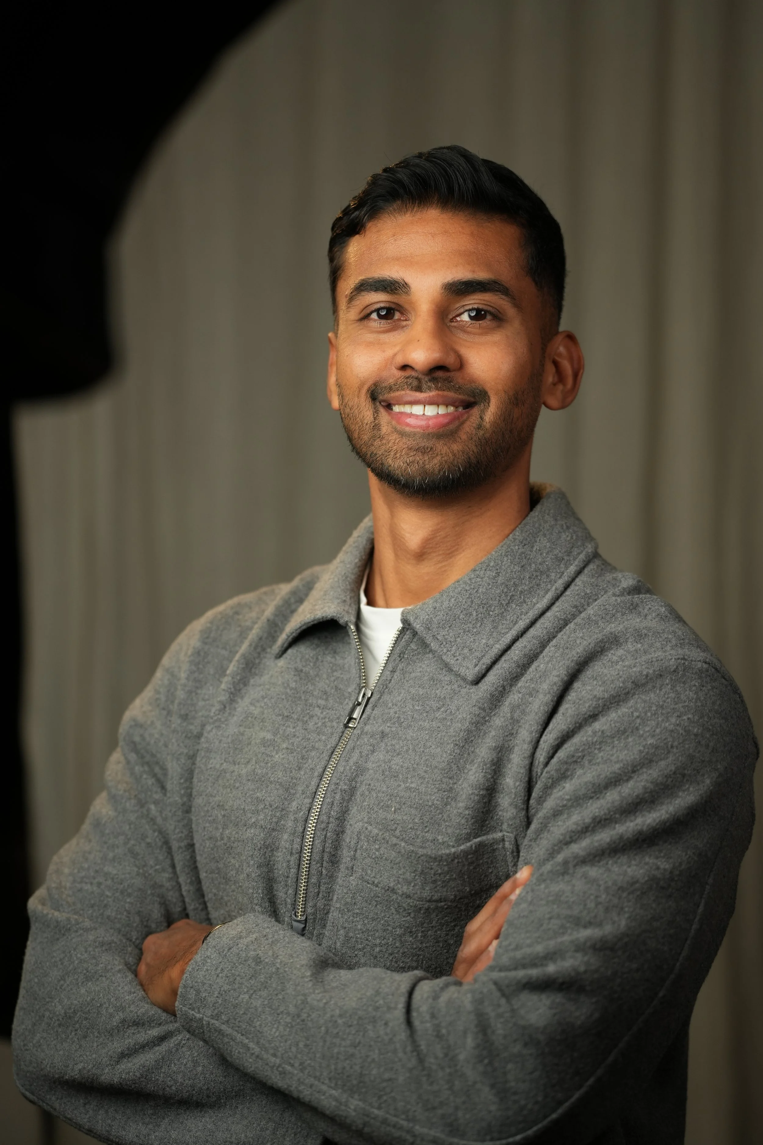 Mann i grå jakke smiler med armene krysset foran en grå bakgrunn.