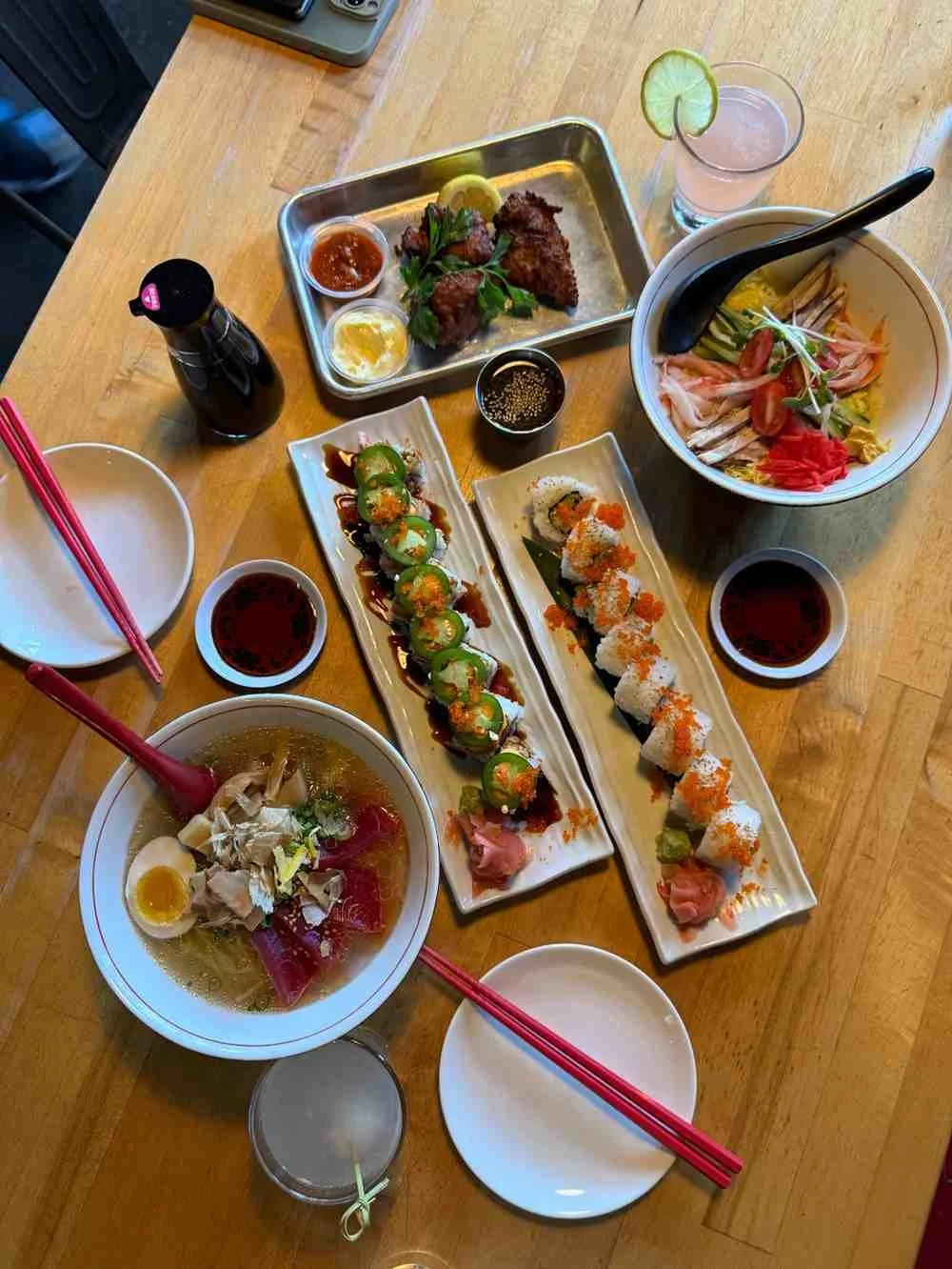 Japanese restaurant table with sushi, yakitori skewers, sashimi bowls and drinks under anime wall screens