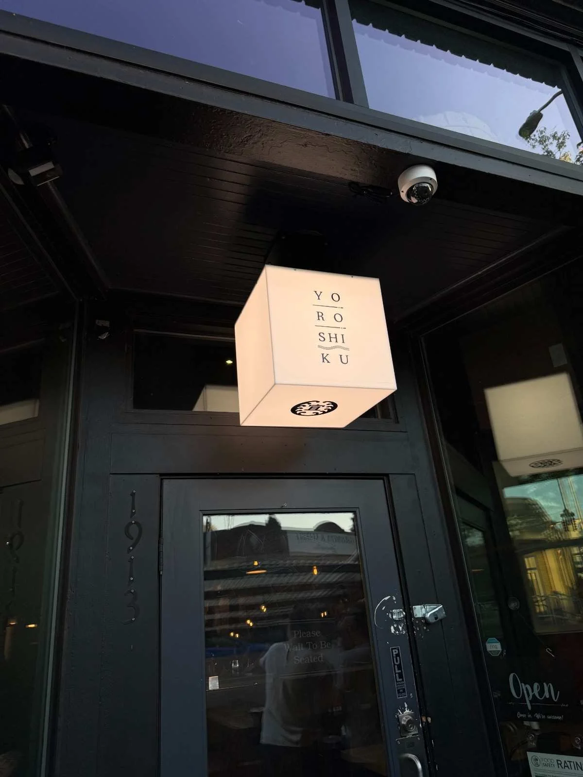 Yoroshiku restaurant storefront with illuminated cube sign and glass door entrance at evening