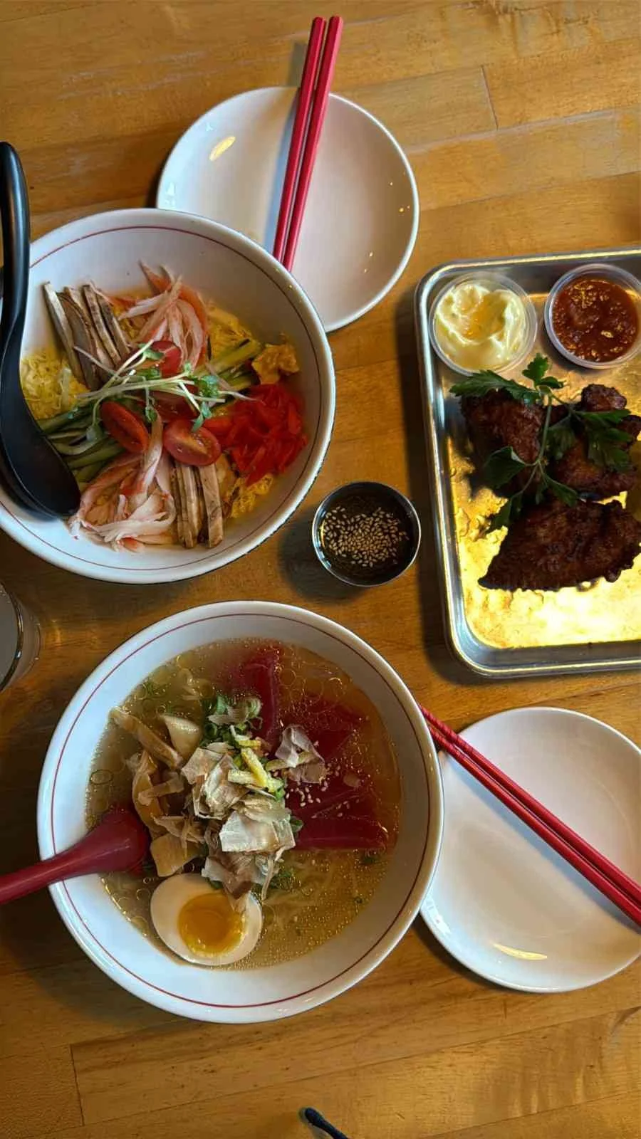 Traditional Japanese meal spread featuring ramen bowls with soft-boiled eggs and vegetables, served with chopsticks and a side dish of meat and rice