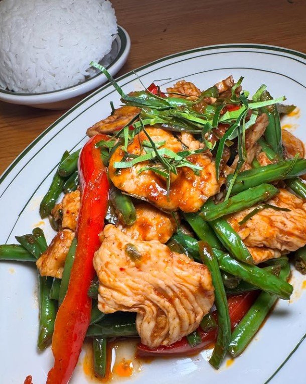 Spicy chicken stir-fry with green beans and red bell peppers on a plate, served with a side of white rice.