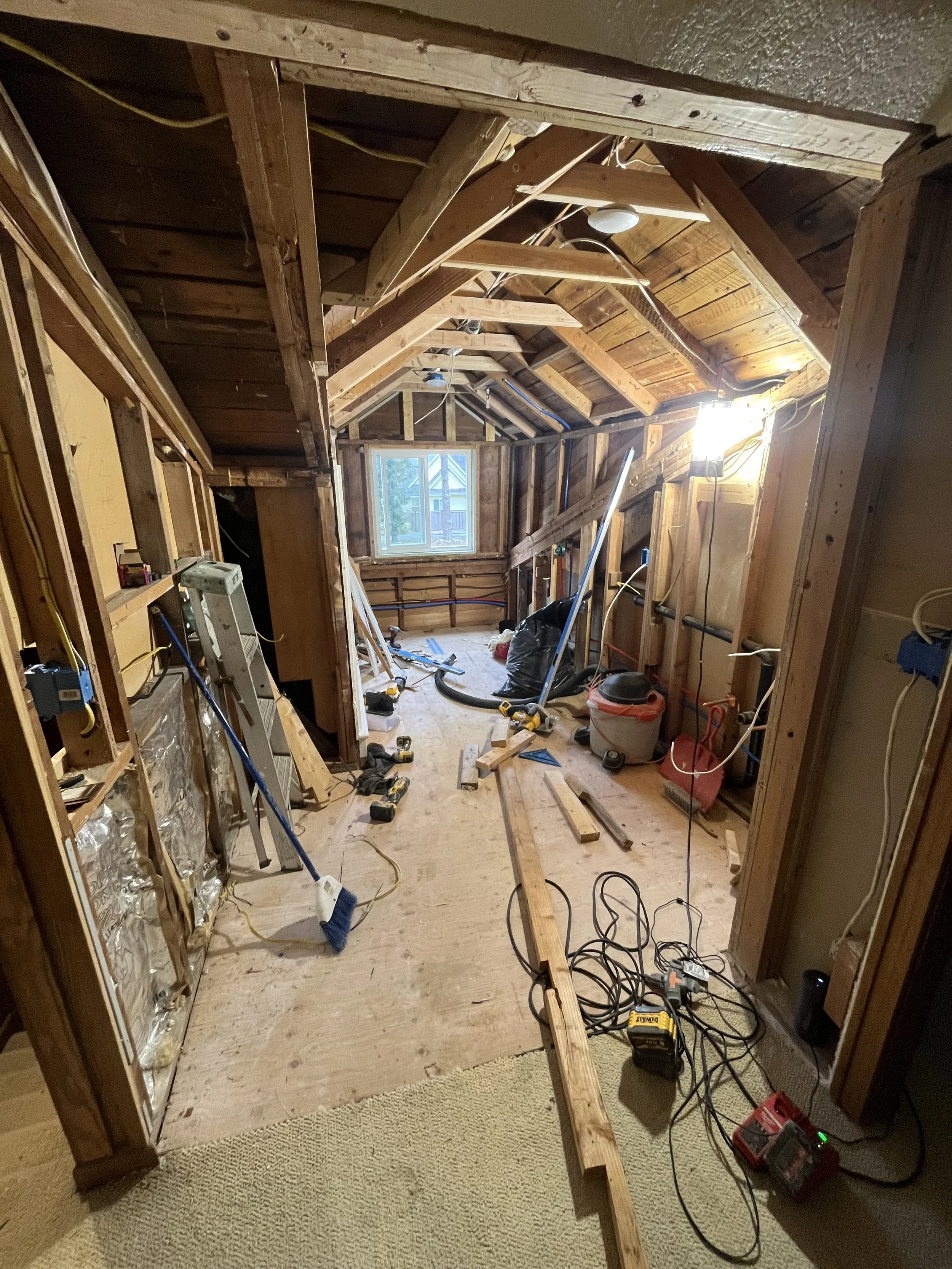 Interior of a room under renovation with exposed wooden framing, construction tools, and a ladder.