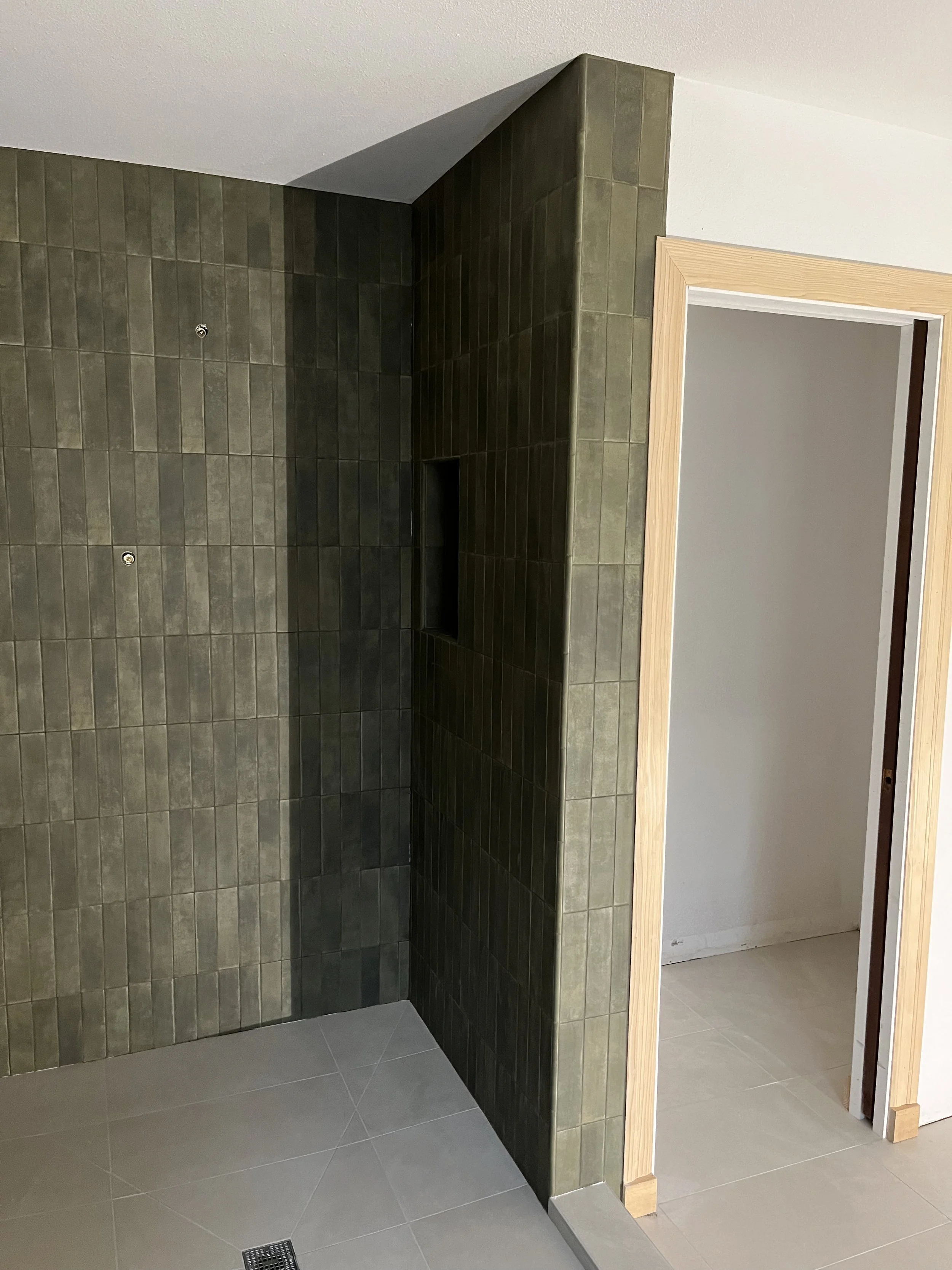 A corner of a room with a partial wall covered in green tiles, a doorway with a wooden frame, and a tiled floor.