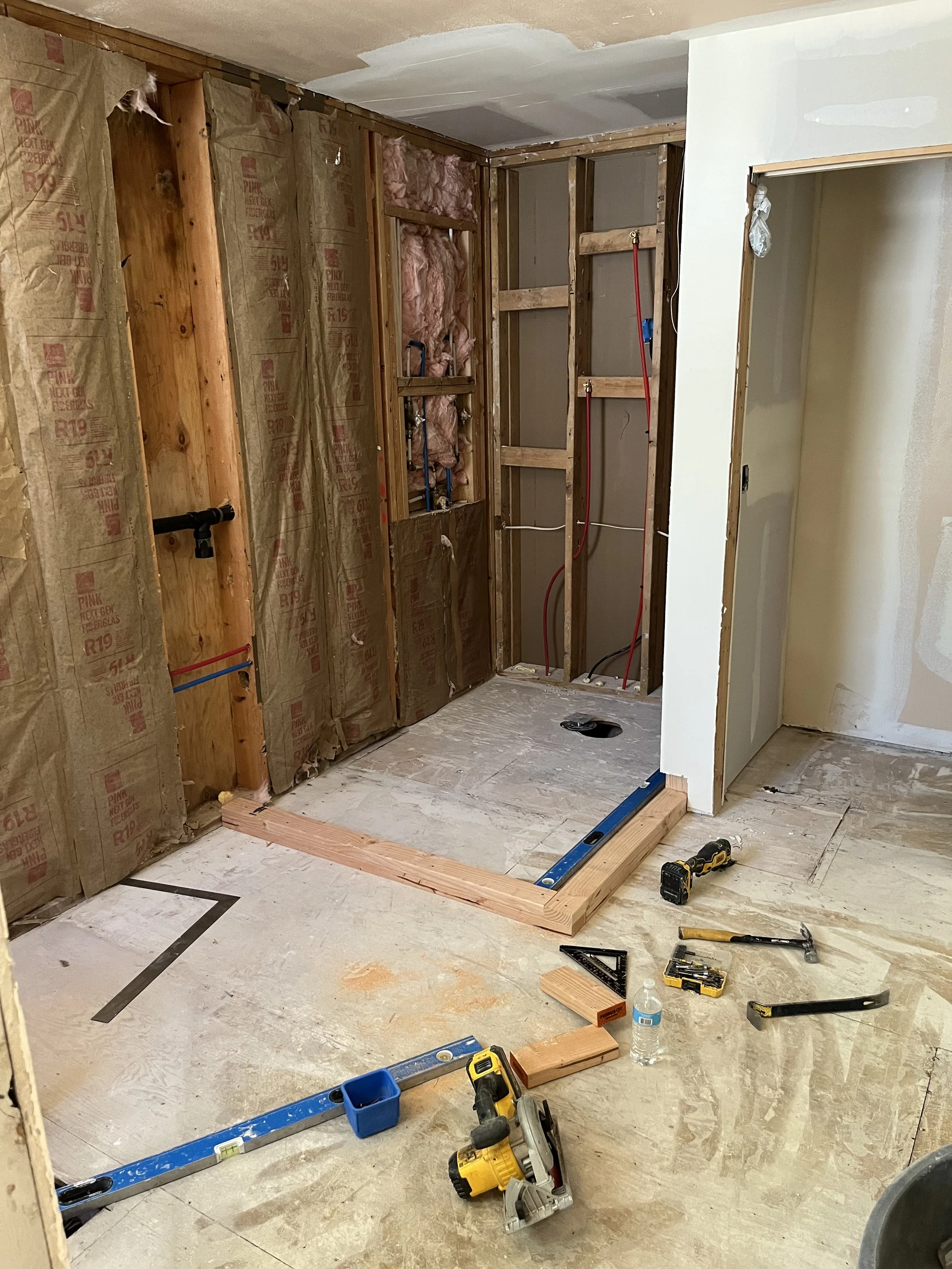 Room under construction with exposed framing, tools, and building materials scattered on the floor.