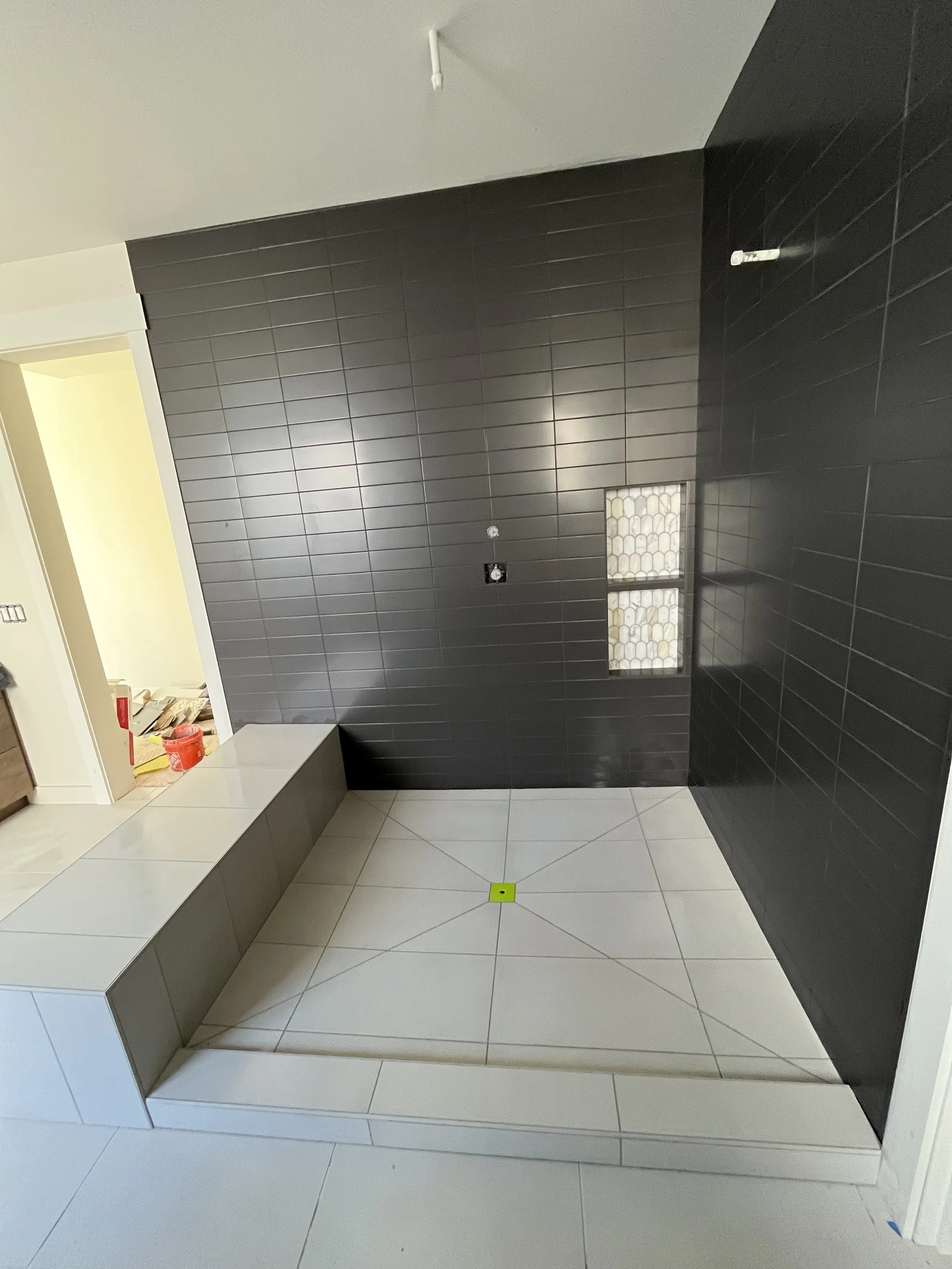 Interior room with dark gray tiled wall, white and gray floor tiles, a small rectangular window, and a yellow marker on the floor.