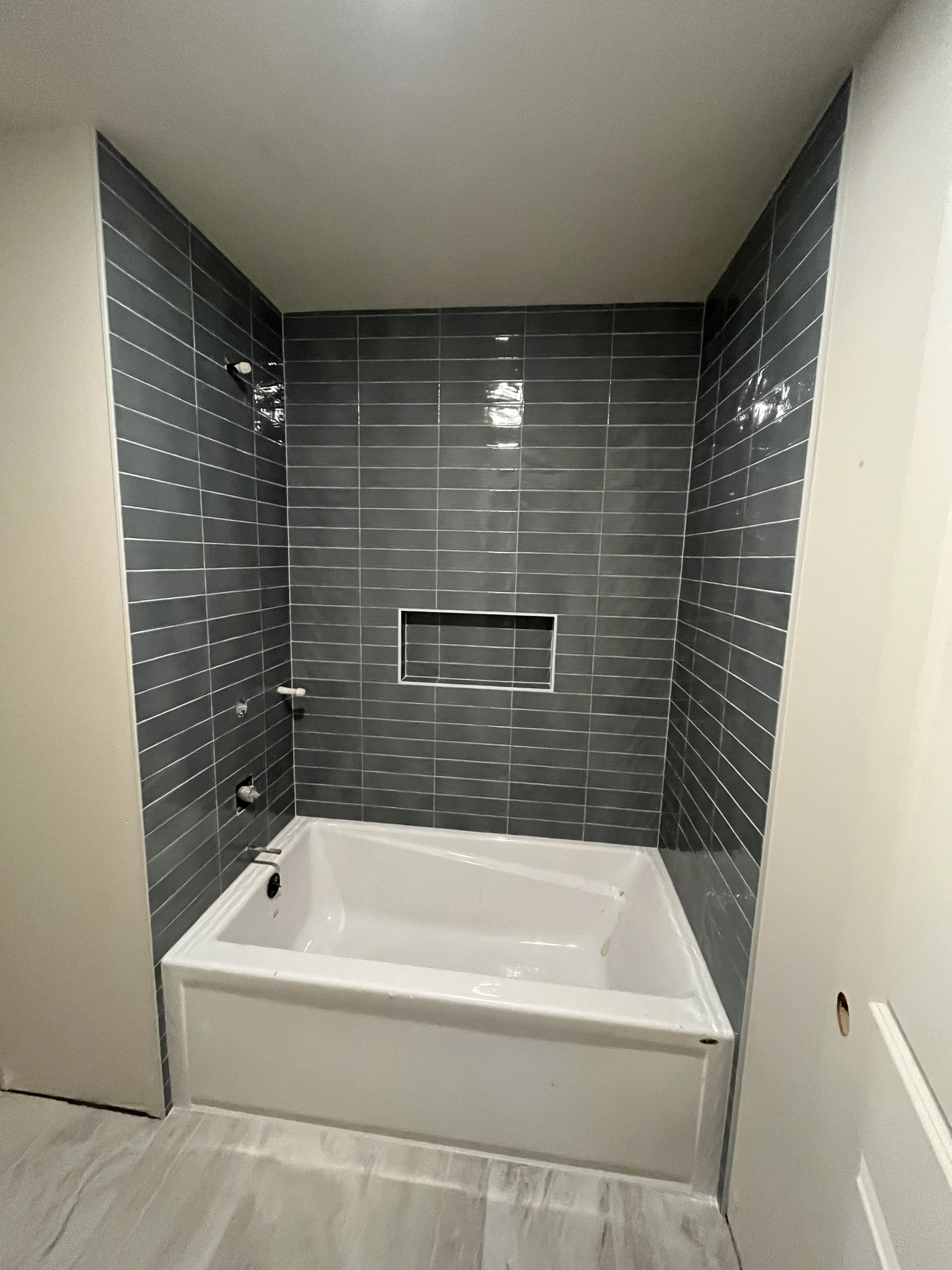 Bathroom shower with dark gray tile walls, a built-in niche, and a white bathtub surrounding the shower area.