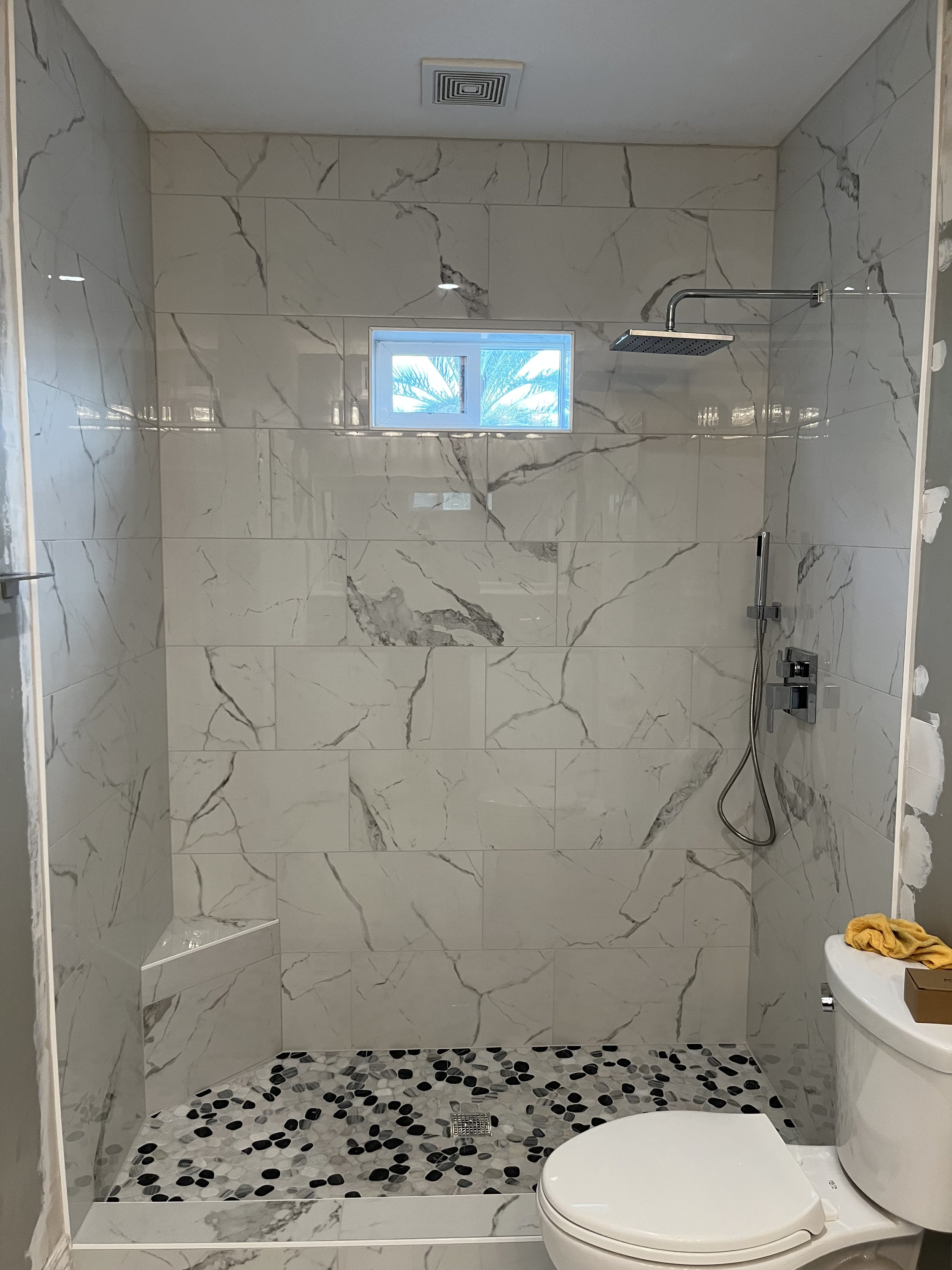 Modern walk-in shower with marble wall tiles, a rainfall showerhead, a small window, and a separate toilet in a bathroom.