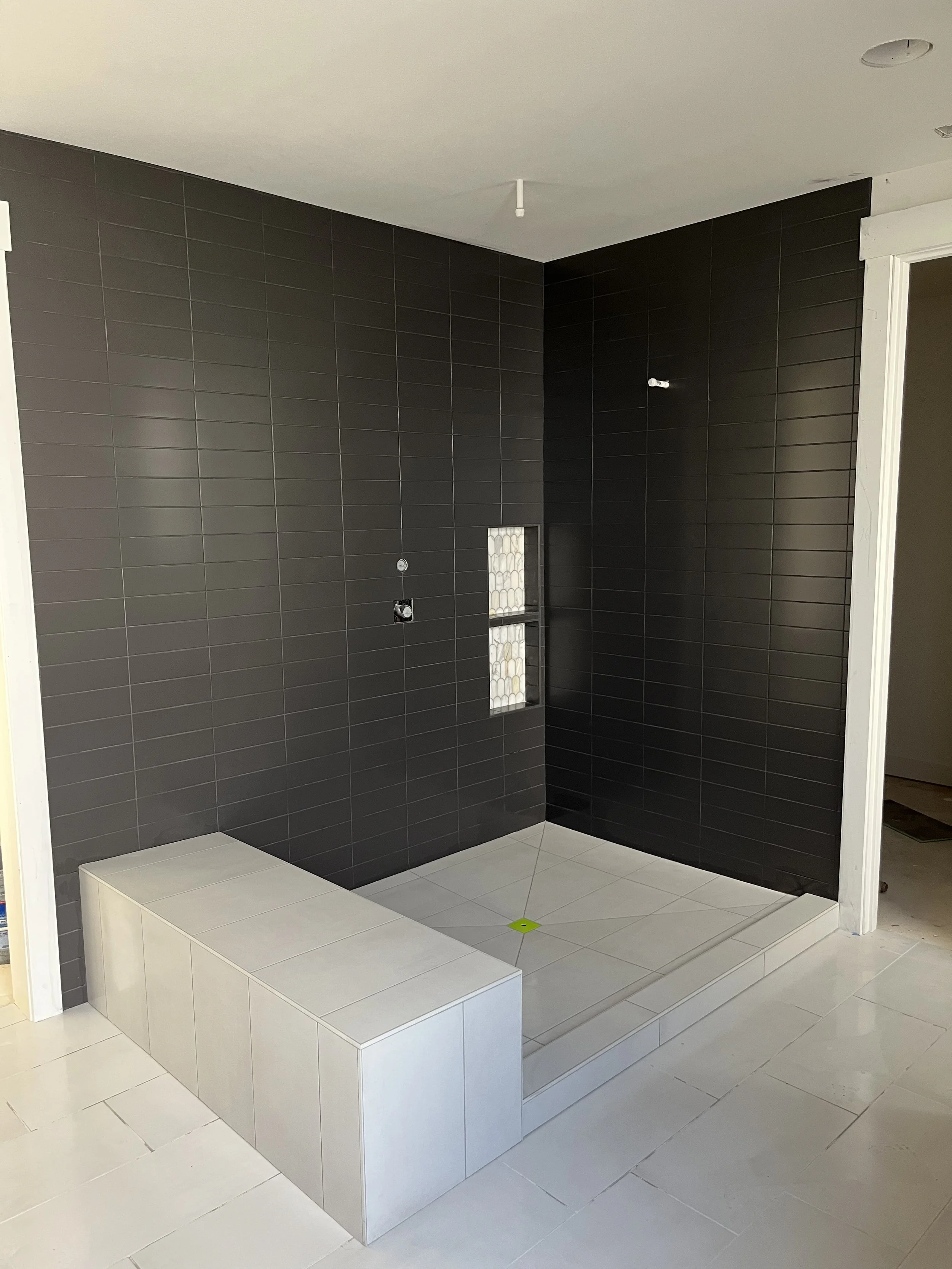 Bathroom under construction with black tiled walls, a white tiled platform, and a small recessed shelf with decorative tiles.