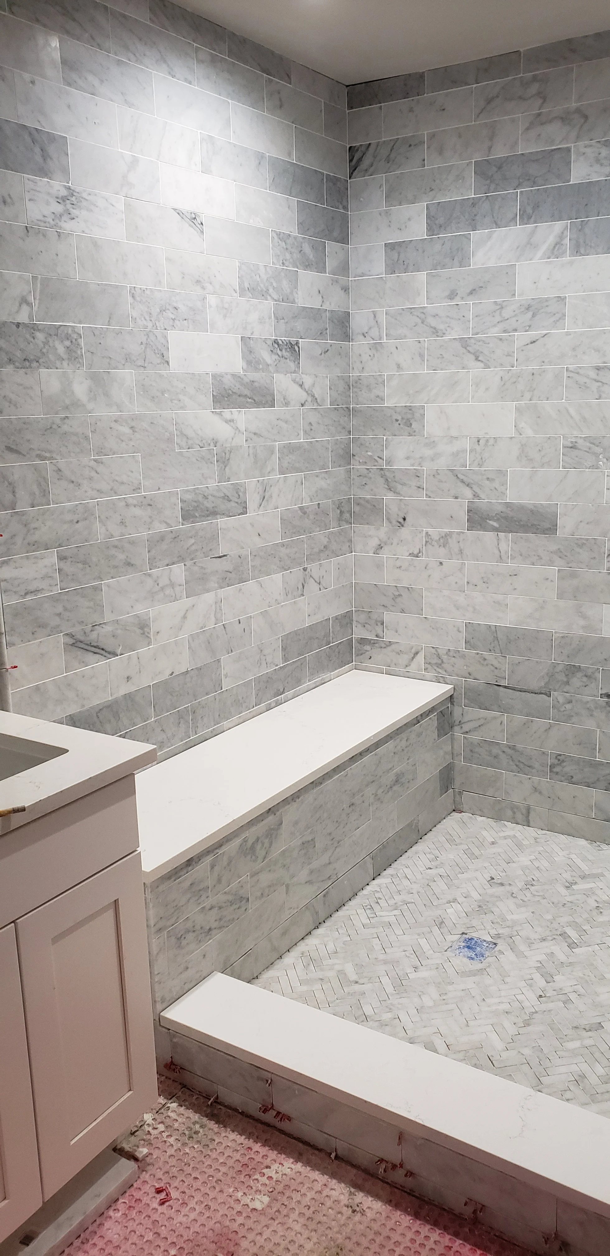 A bathroom with marble tile walls and a marble bench, with a partially finished floor and a pink cabinet.