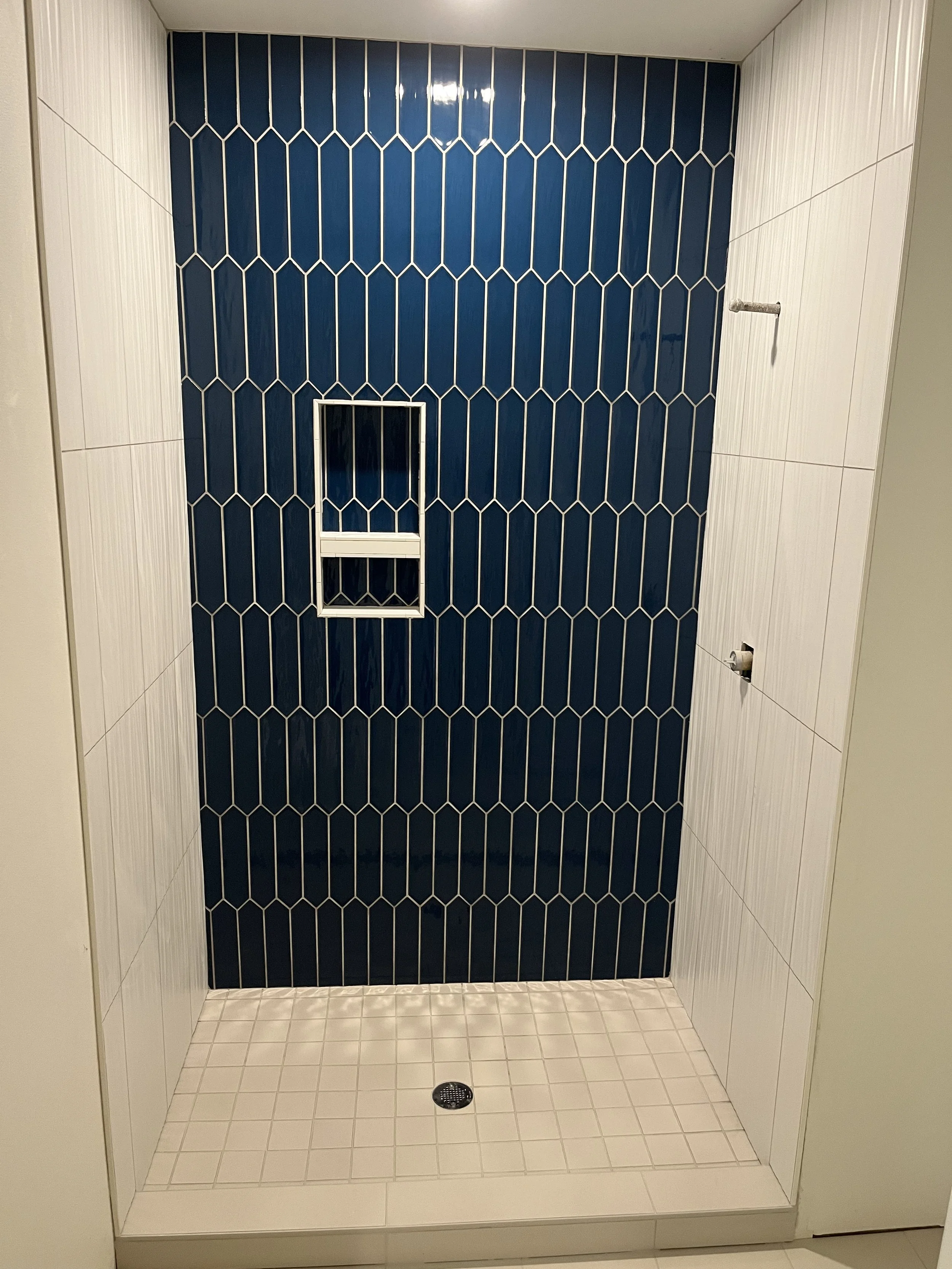 Empty shower stall with blue tiled wall, white side walls, and a drain on the floor.