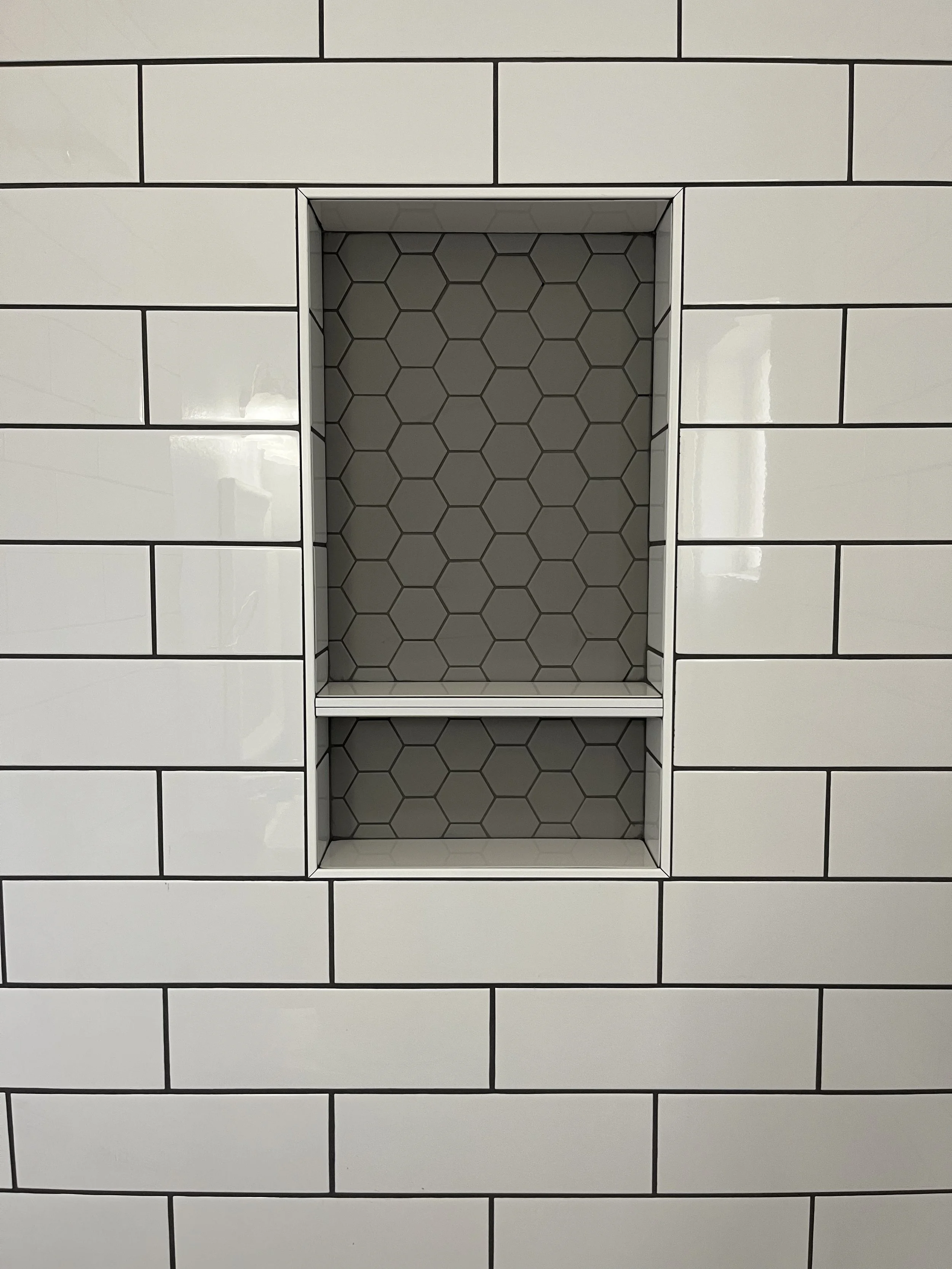 A recessed shelf within a white tiled wall, with a hexagon patterned interior.