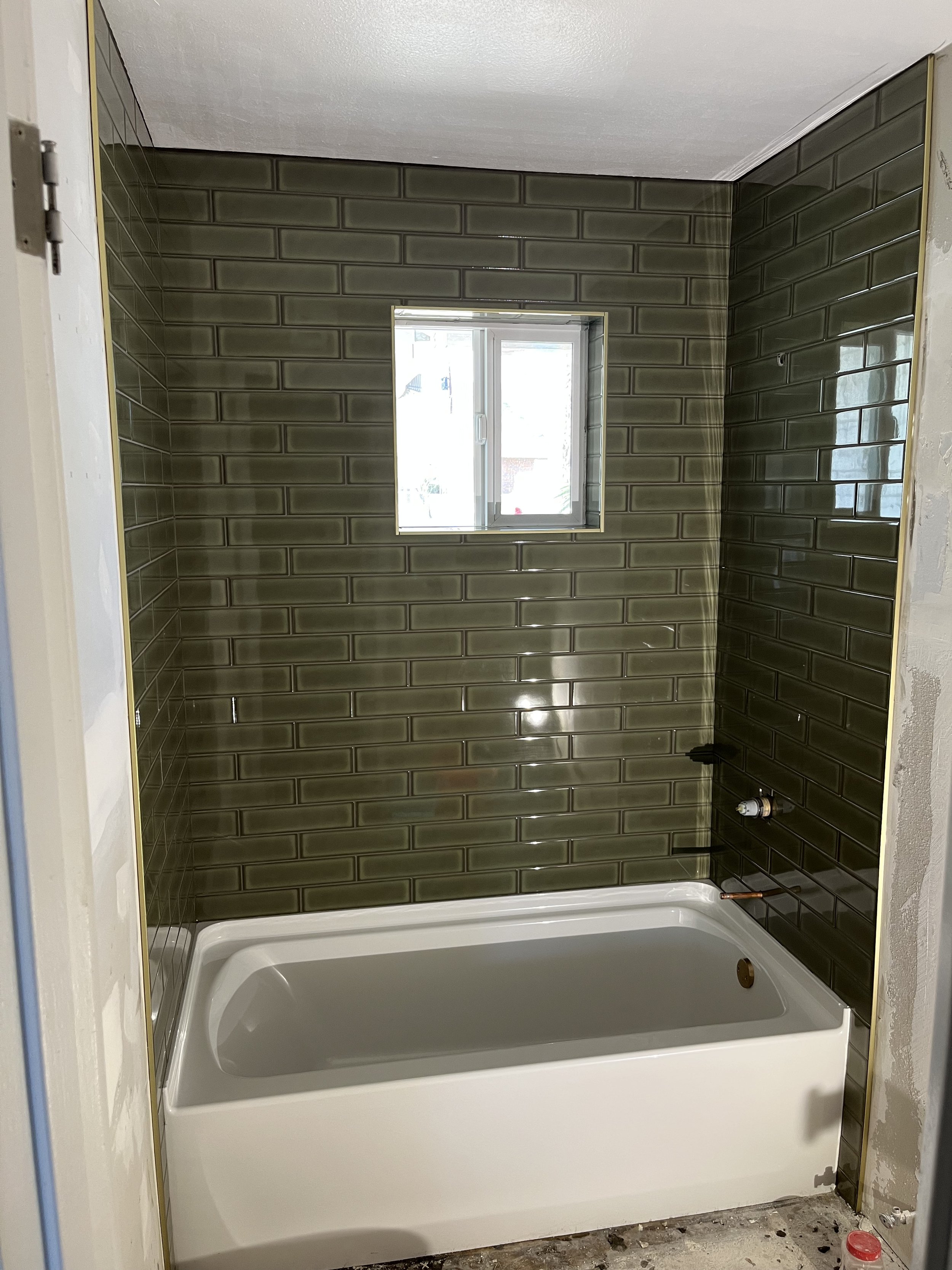 Bathroom with dark green subway tiles on walls, a small window, and a white bathtub under construction with fixtures not yet installed.