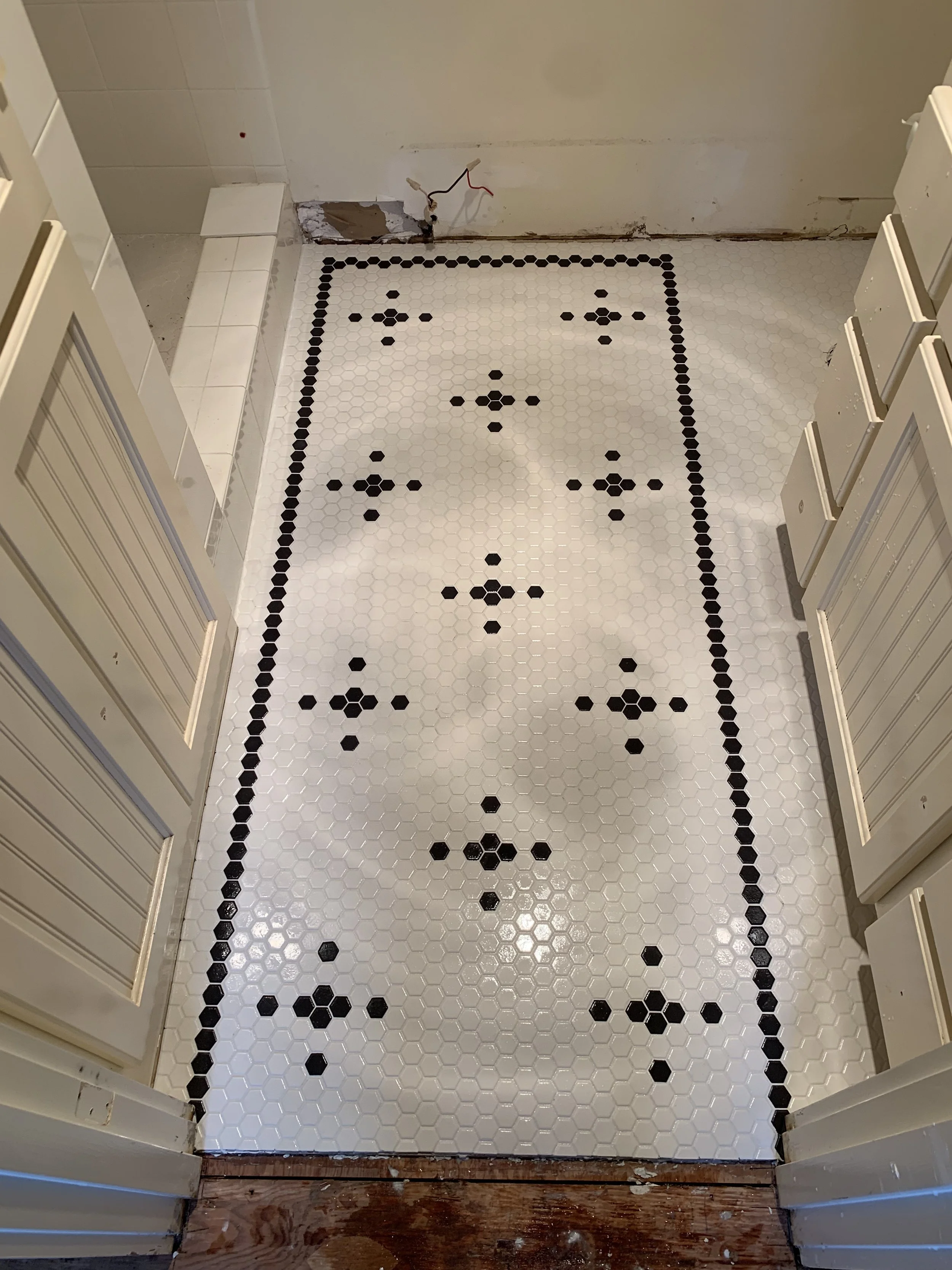 Kitchen floor with white hexagonal tiles and a black diamond pattern border and design in the center, with some construction or renovation work visible at the edges.