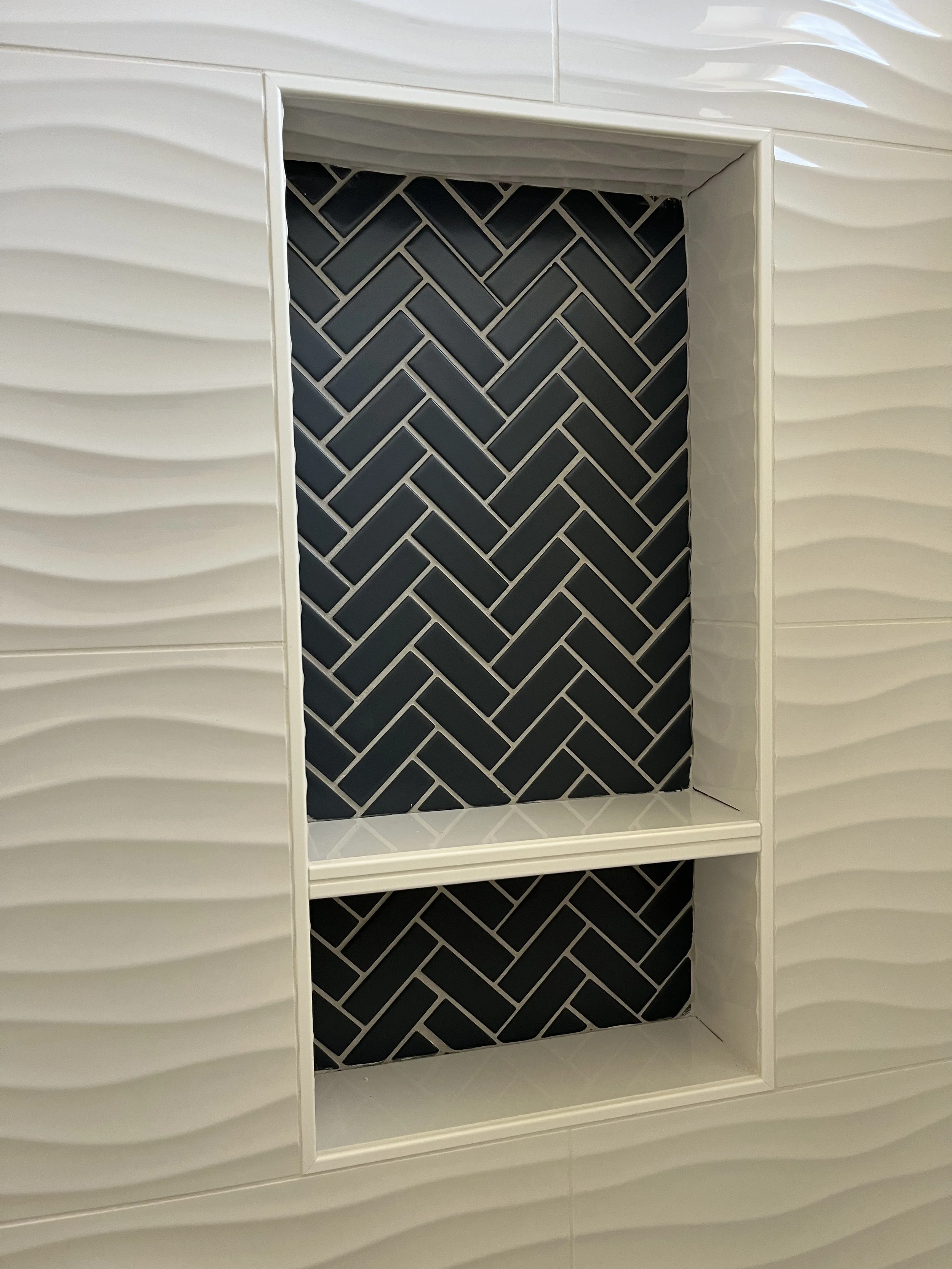A white textured surface with a black herringbone tile pattern inside an open shelf or niche.