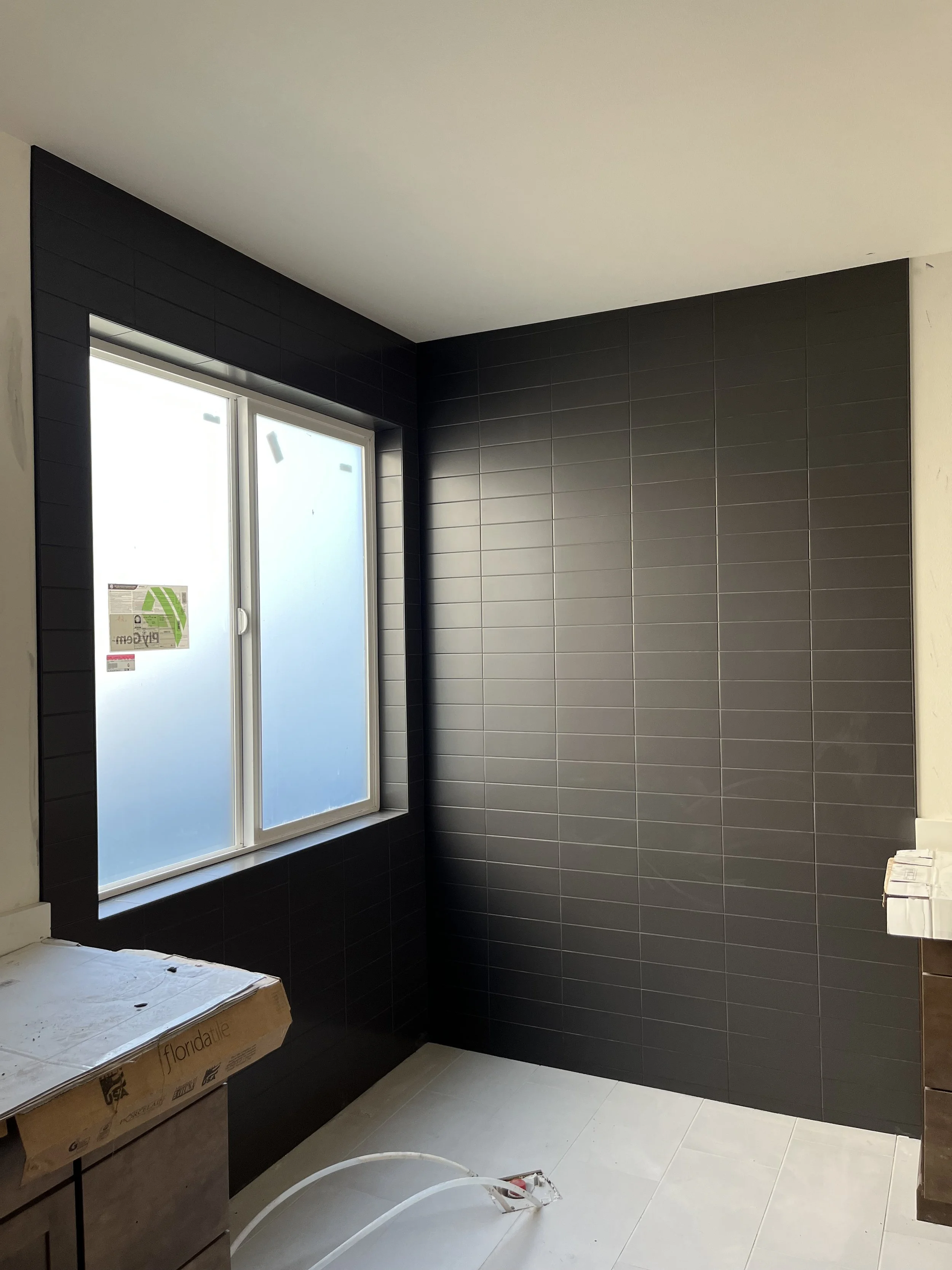 A room under construction with black tiled walls, a large window, and some construction materials on the floor.