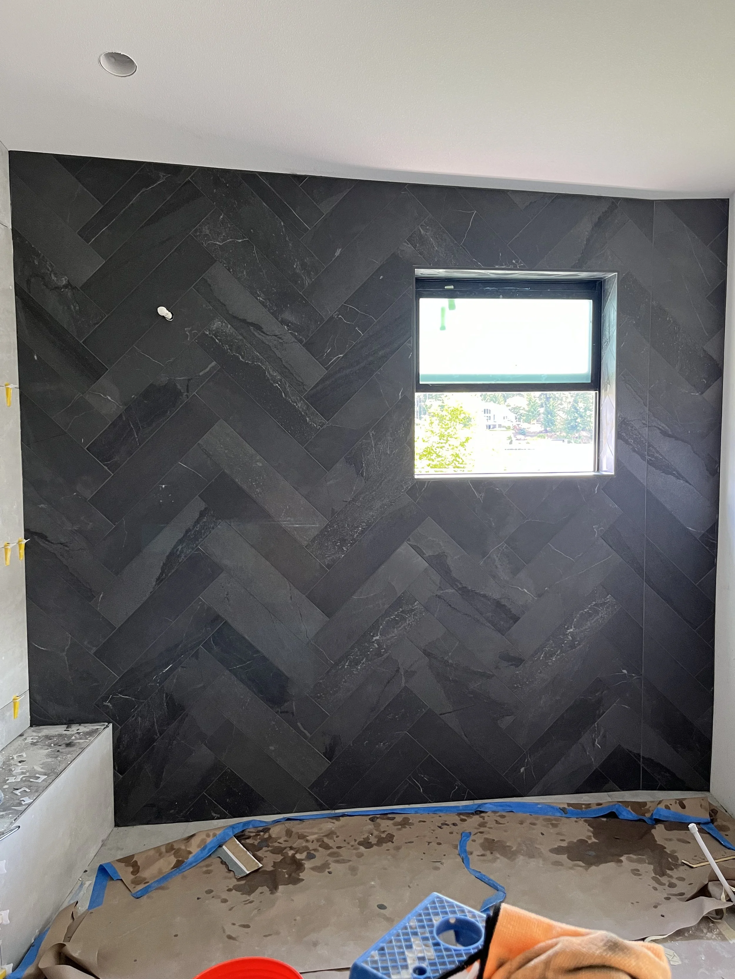 Interior view of a room under construction with a new black tile wall, a small window, construction tools, and supplies on the floor.