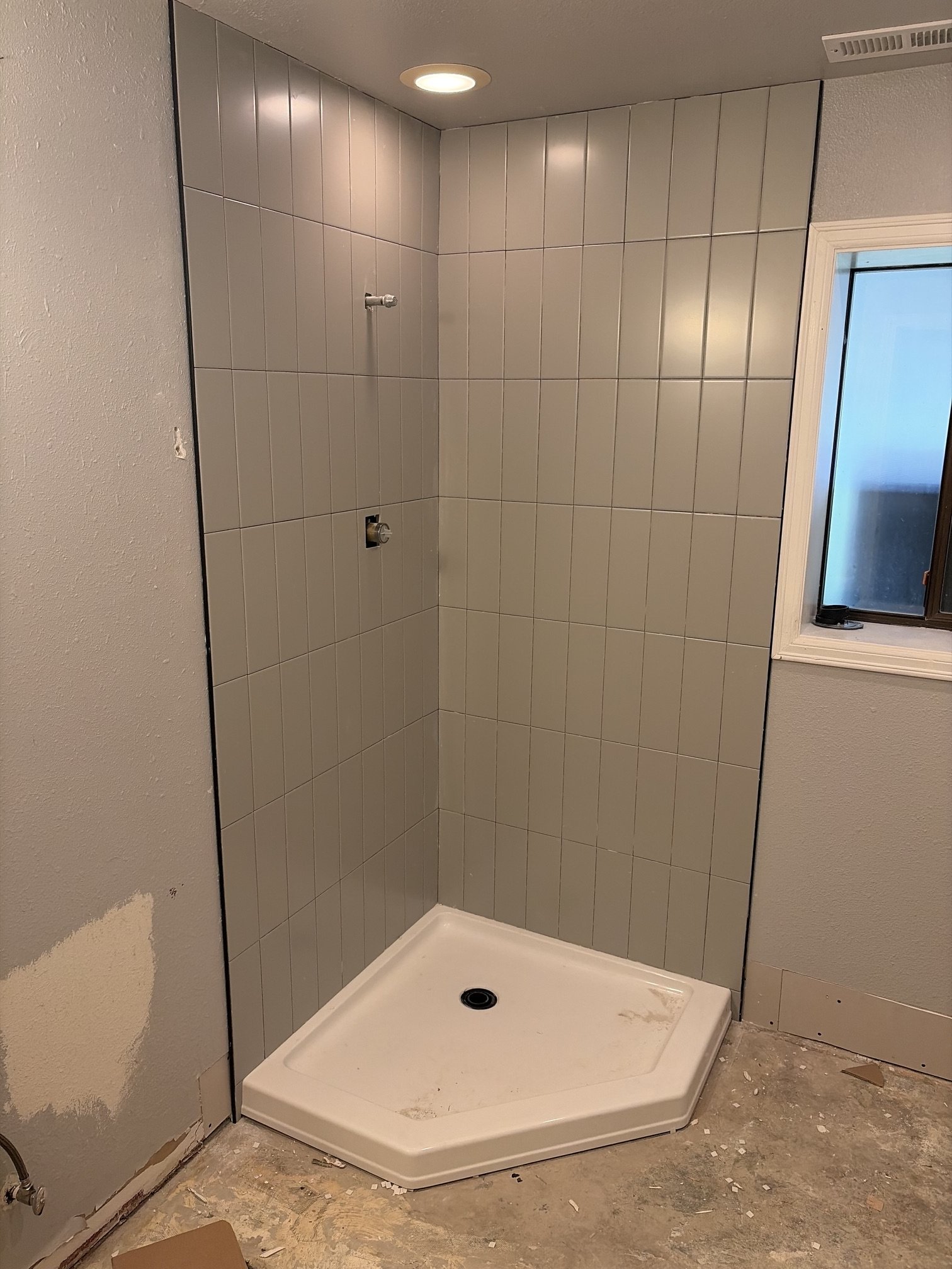 A new shower stall installed in a bathroom, with gray tile walls, a white shower base, and a partially unfinished wall.