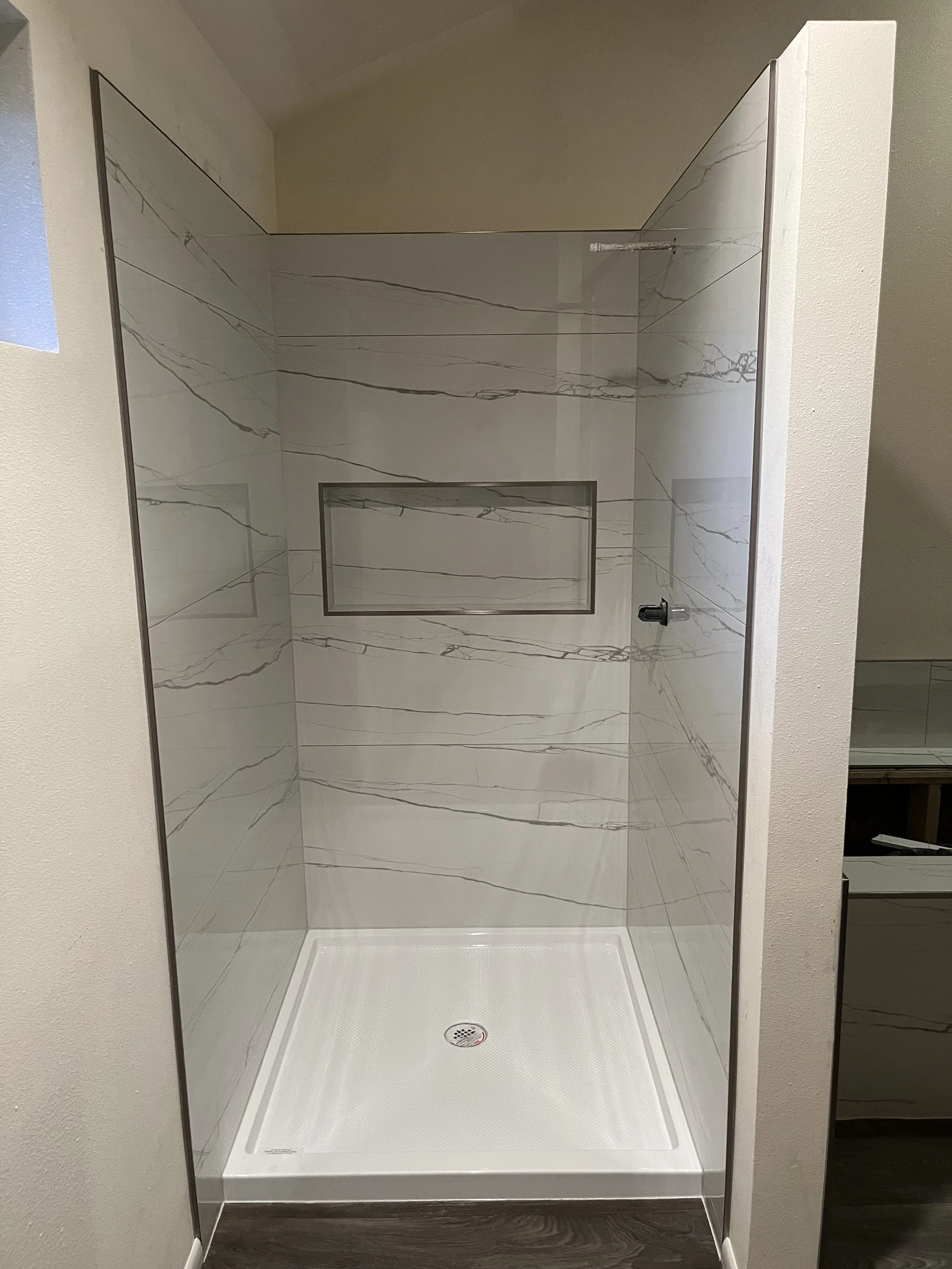 Empty walk-in shower with marble walls, a built-in niche, and a white shower base, in a modern bathroom.