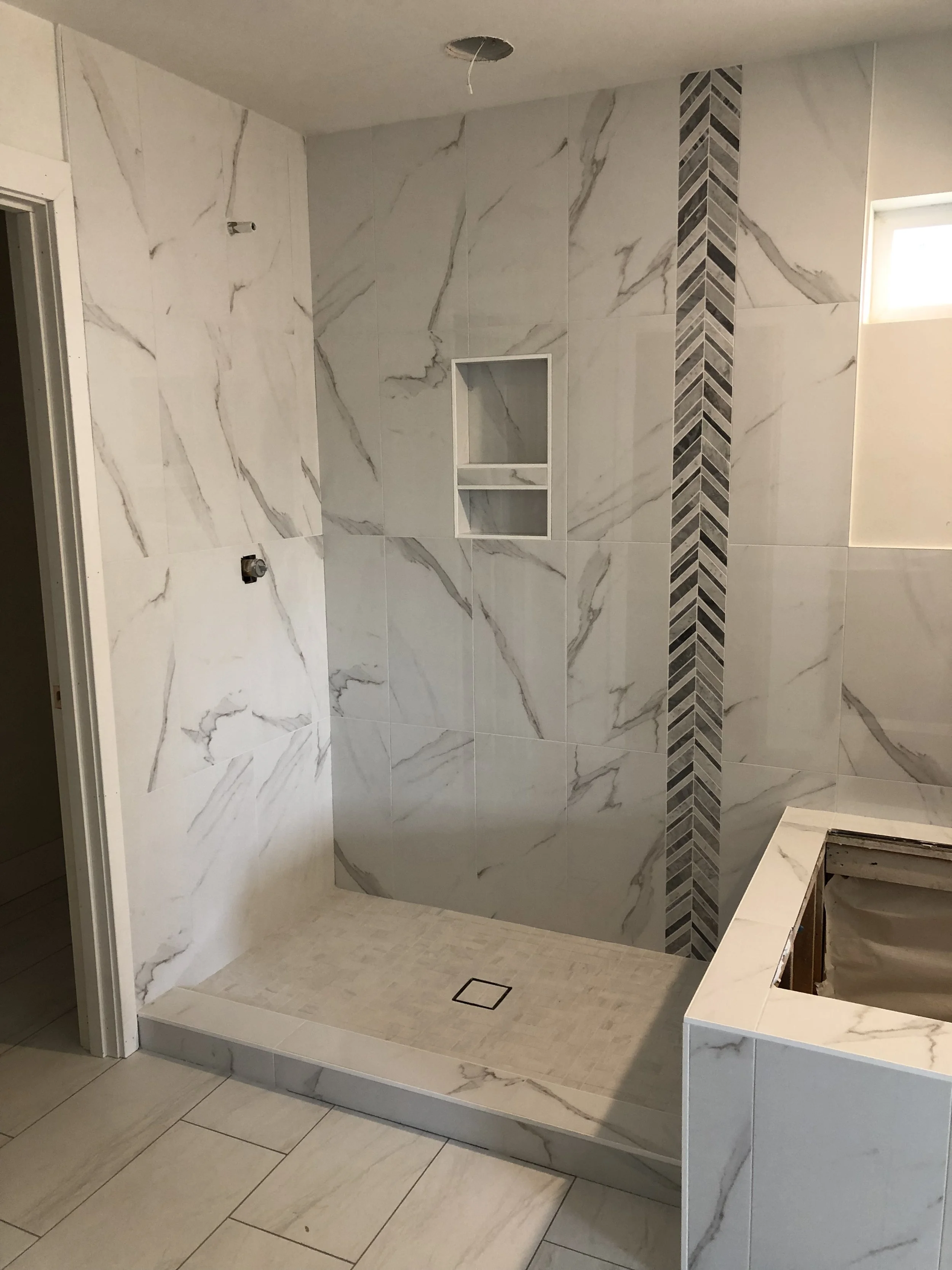 Empty bathroom shower with white marble tiles and a built-in niche for soap or shampoo, and a small window on the right.