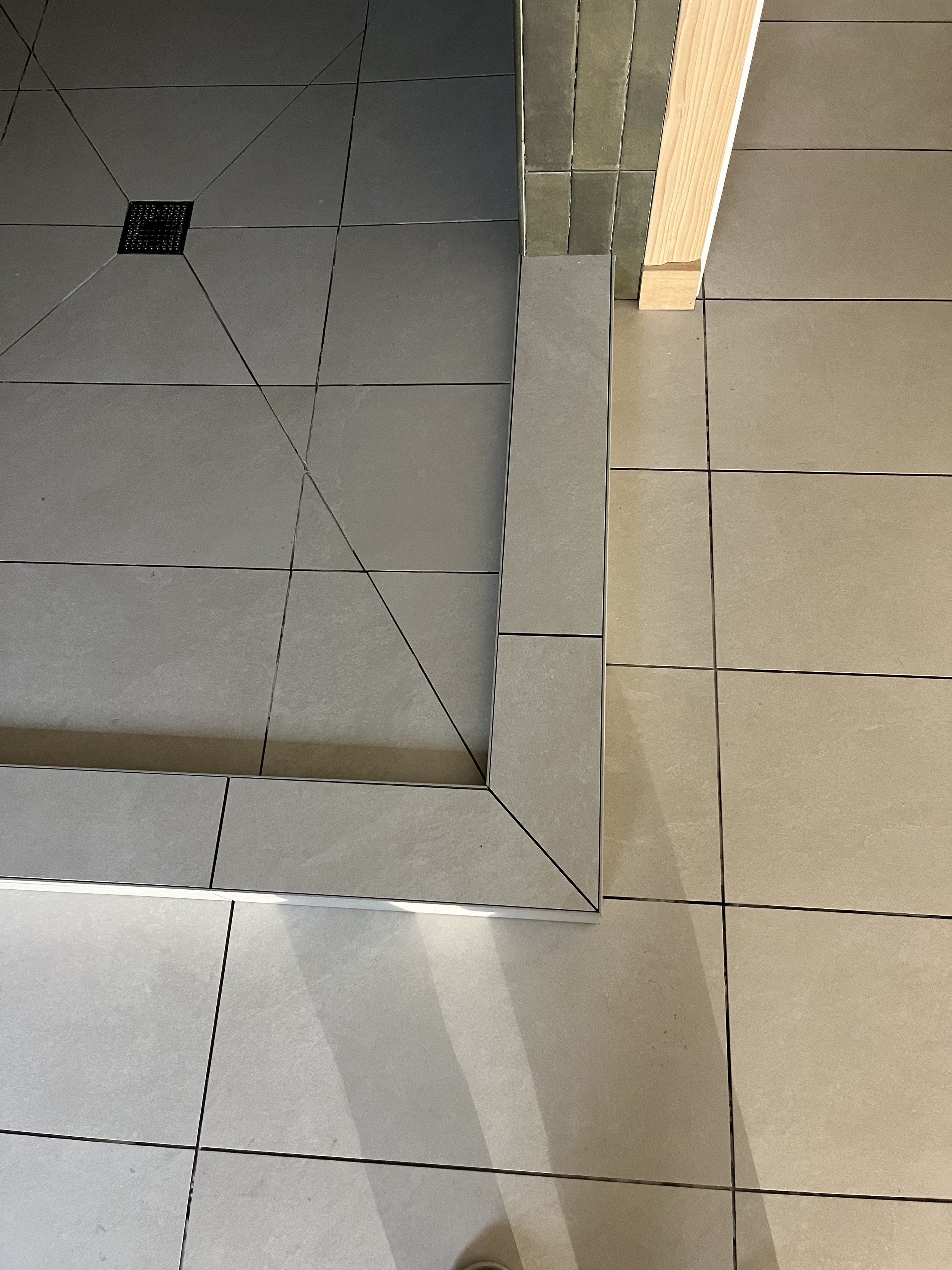 Close-up of tiled floor with gray, beige, and green tiles, and a small drain on the gray tiles.