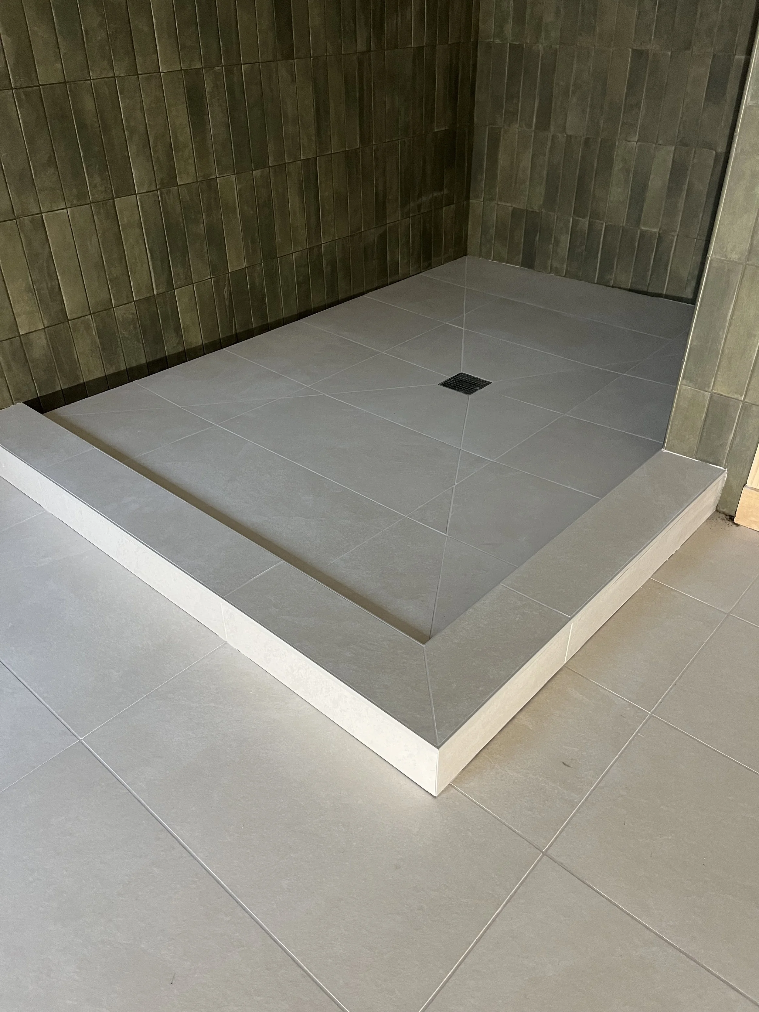 Shower area with dark brown wall tiles and light gray floor tiles, including a drain in the center.