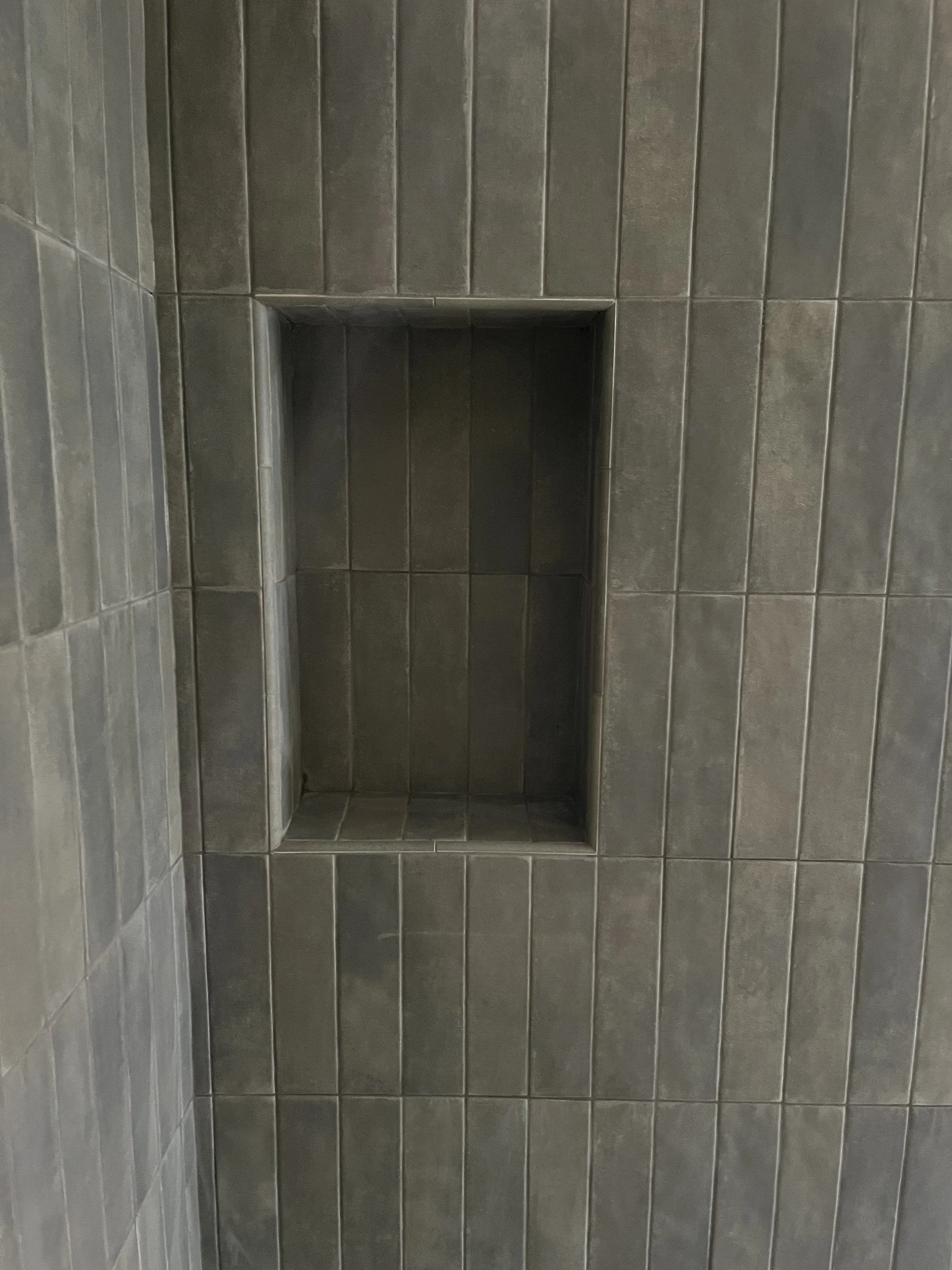 A shower with dark gray tiled walls featuring a built-in wall niche with no items inside.