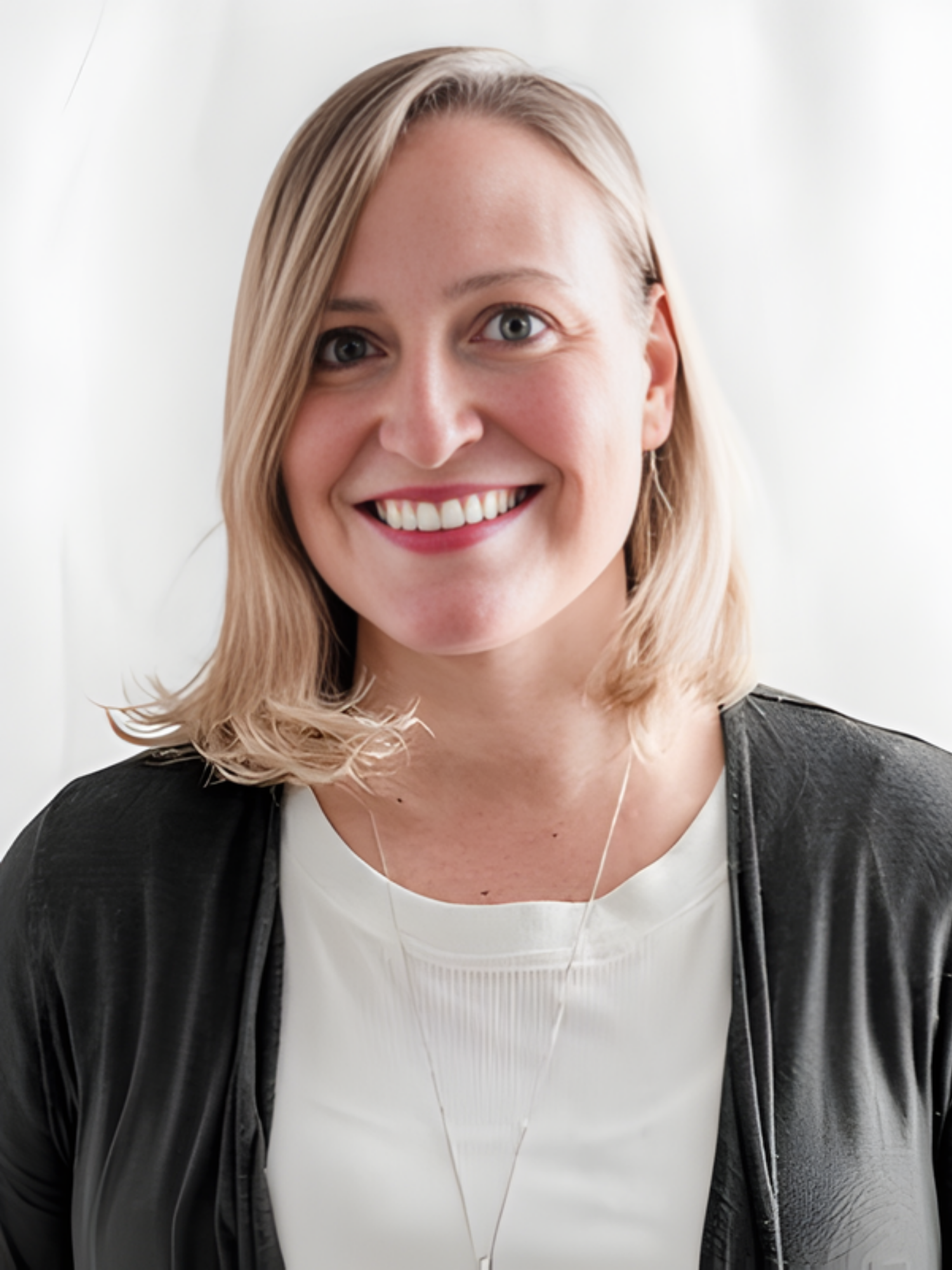 Smiling woman with shoulder-length blonde hair, wearing a gray cardigan and white top, standing in front of a white background.