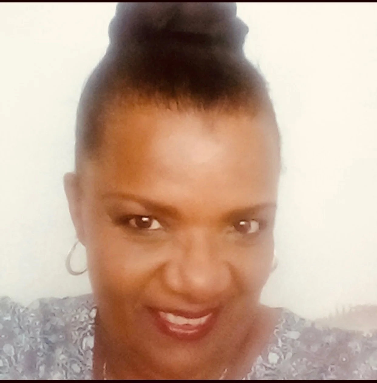 Portrait of a woman with dark hair styled in an updo, wearing hoop earrings and smiling.