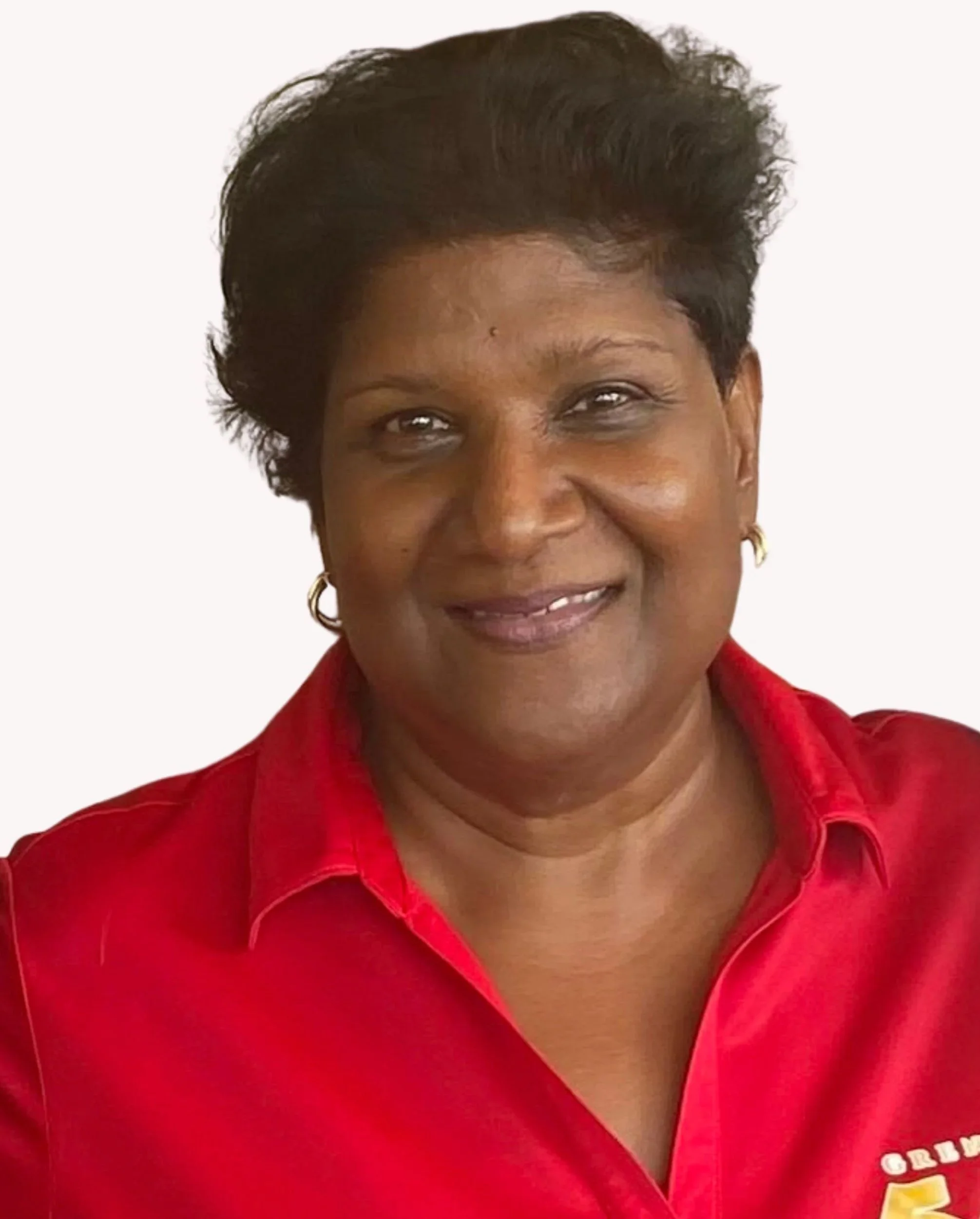 A smiling woman with short black hair, wearing a red collared shirt with gold hoop earrings, standing against a white background.