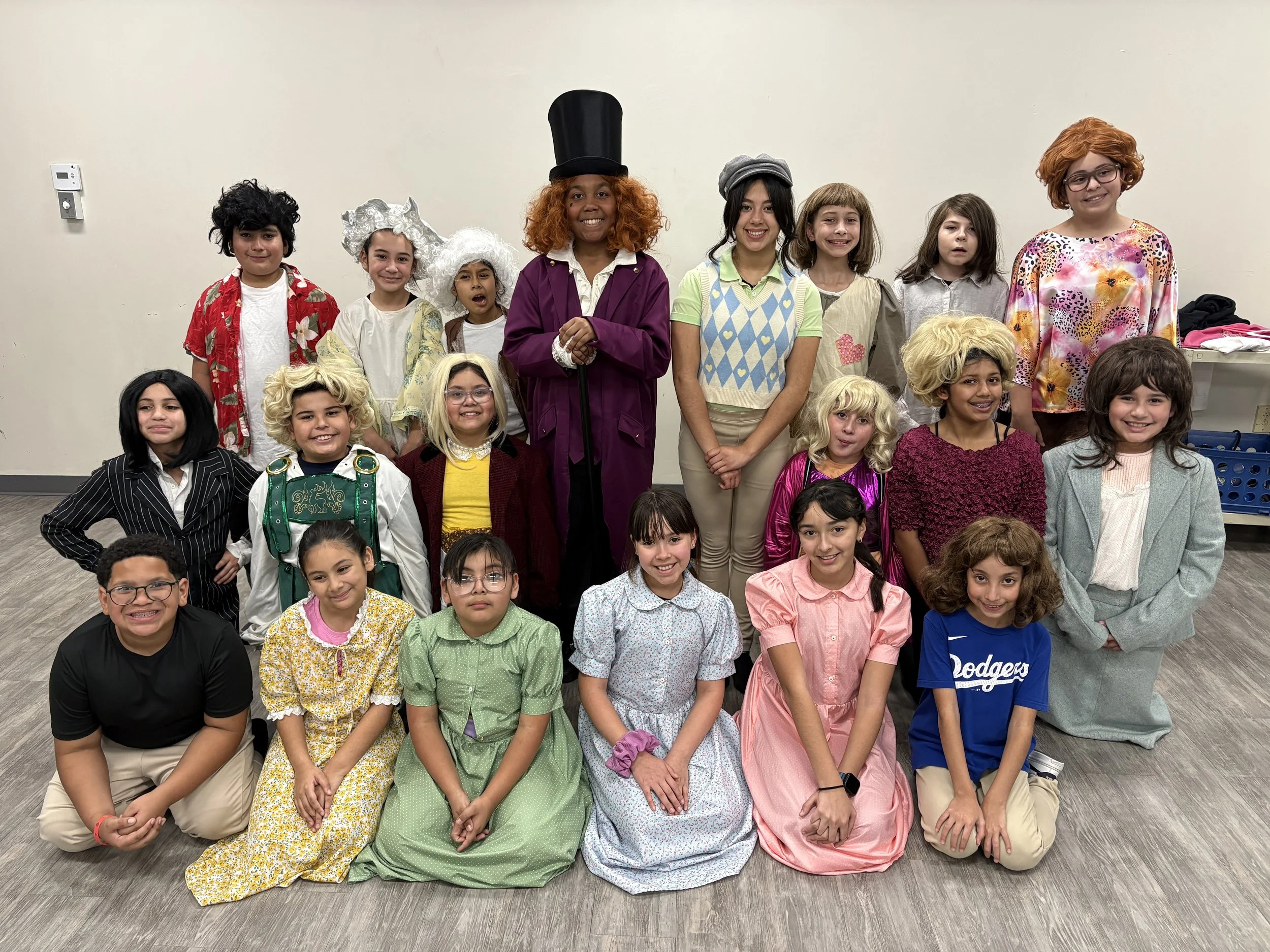 Group of children dressed in costumes from the musical 'Willy Wonka' posing for a photo indoors.