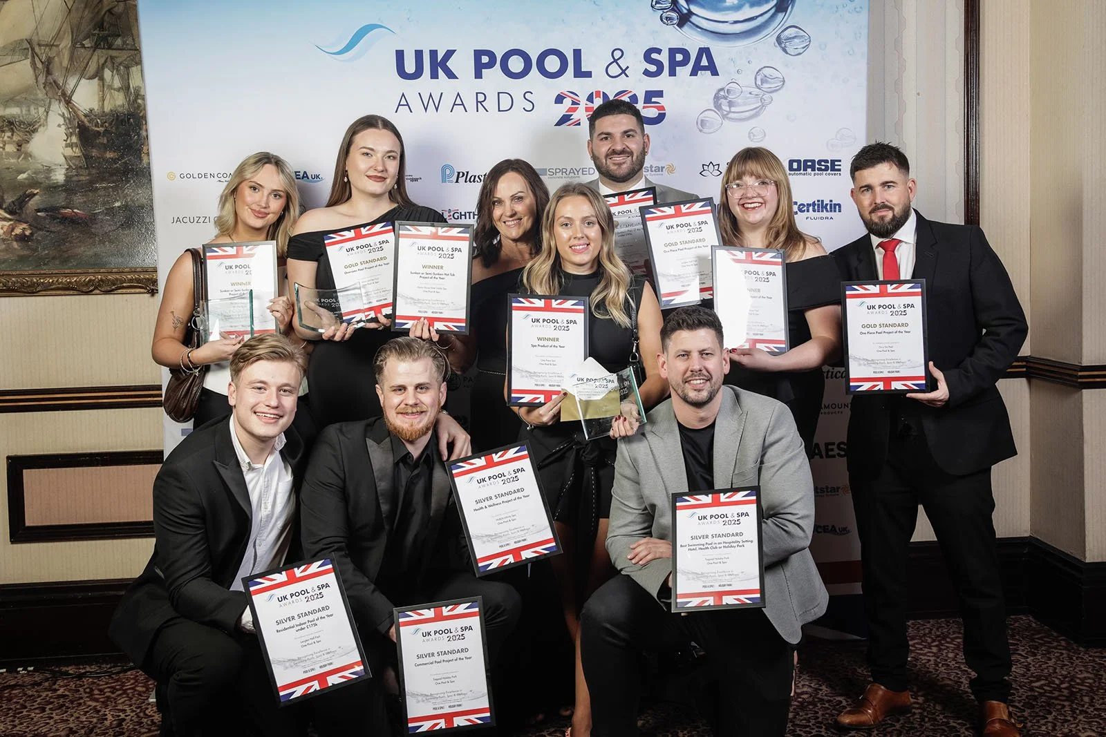 Group of eleven people at the UK Pool & Spa Awards 2023, holding certificates and trophies, posing for a photo in a formal event setting.
