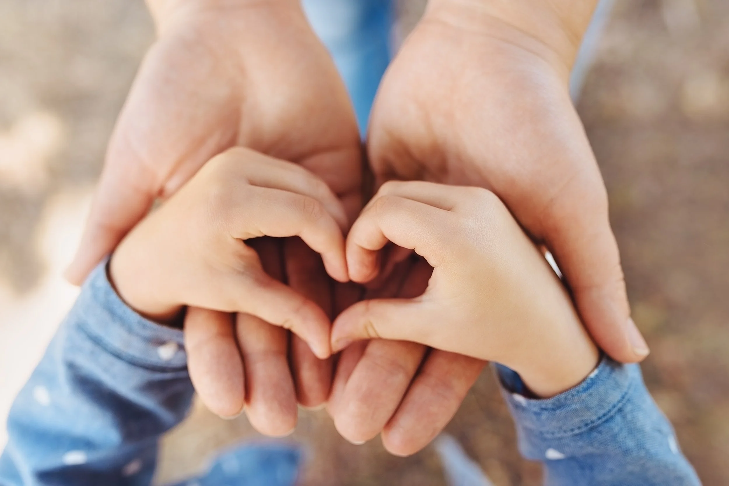 Two pairs of hands, one adult and one child, forming a heart shape with their fingers.